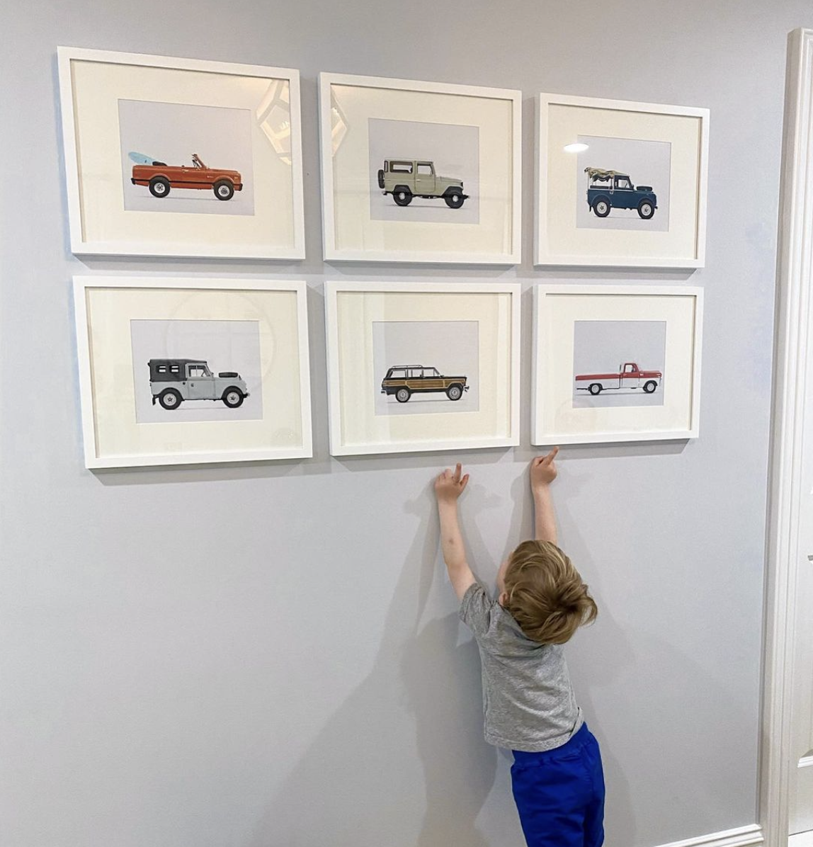 A young boy looking up at six framed pictures of vintage trucks on a wall.