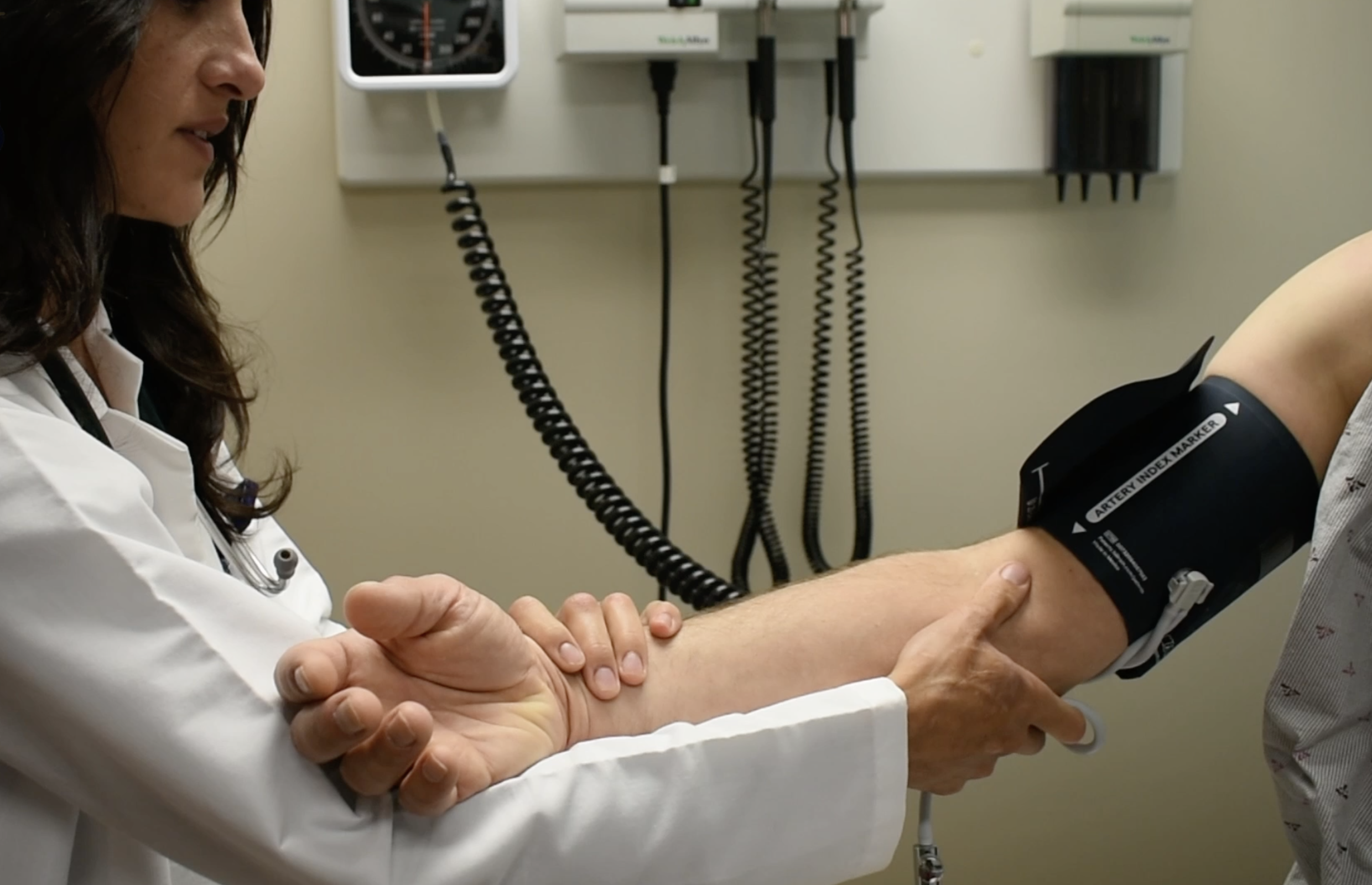 A female doctor (Dr. Mary Zrull of Lifelong Medicine, Direct Primary Care) measuring a patient's blood pressure using a sphygmomanometer.