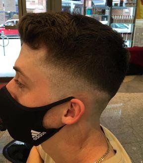Side profile of a young man with a short, faded haircut wearing a black face mask.
