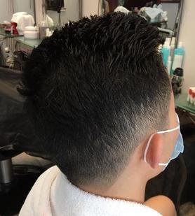 A man with a fresh high fade haircut sitting in a barbershop, wearing a face mask.