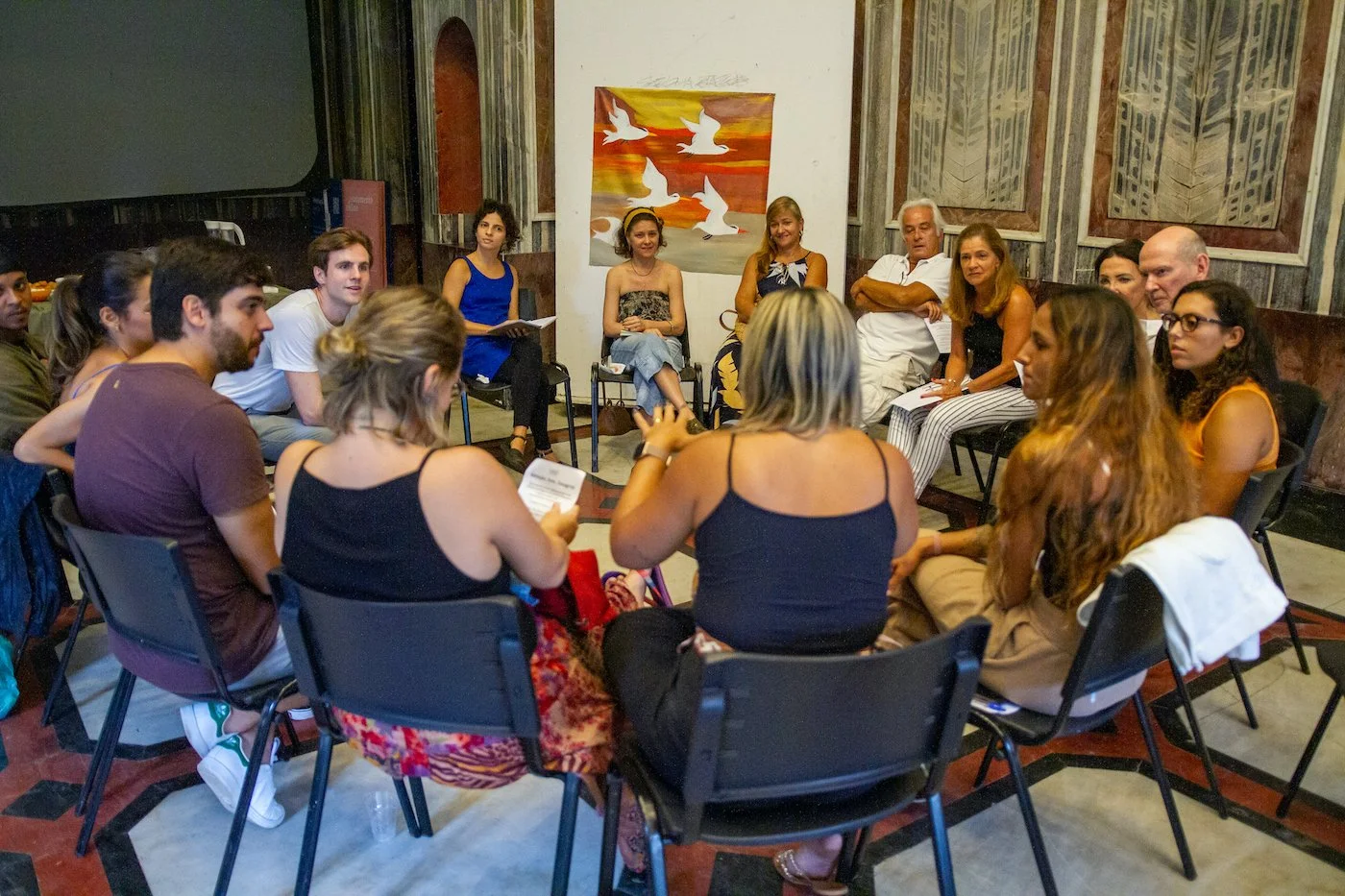Group of people sitting in a circle during a workshop in a room with artwork on the wall.