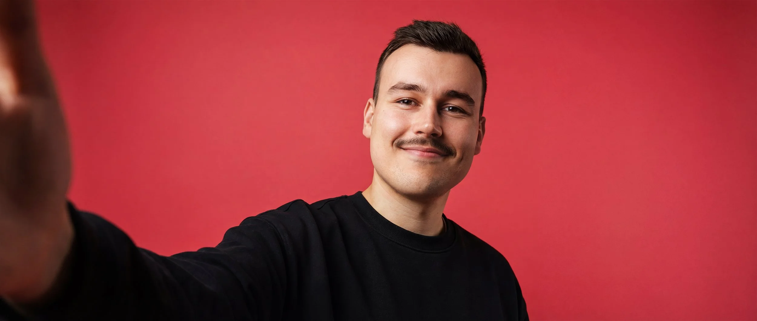 Ein lächelnder junger Mann macht ein Selfie vor einem roten Hintergrund.