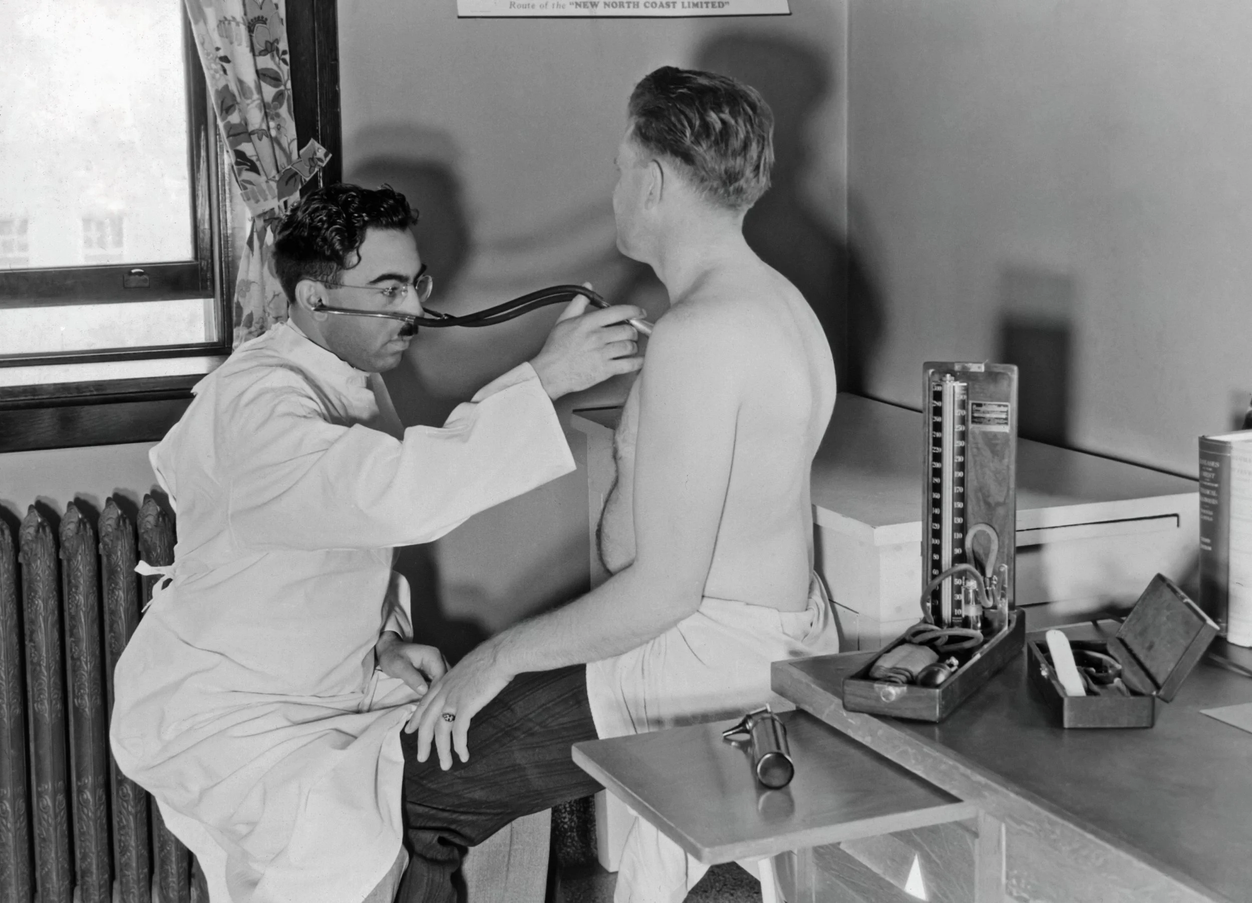 Doctor using a stethoscope on a patient's back in a 1940s medical exam room with vintage medical equipment.