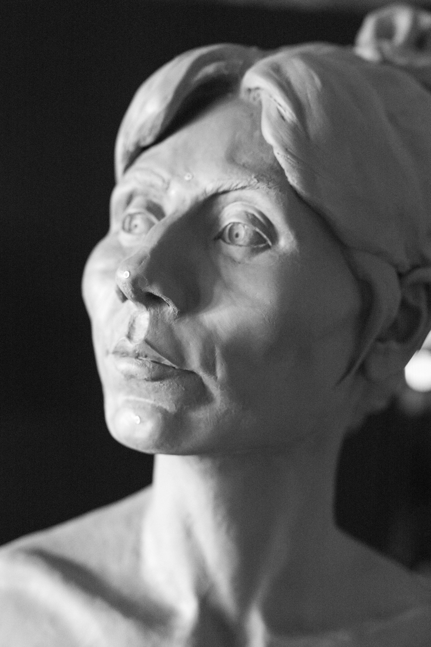 Close-up of a classical marble bust of a woman, showing her face and part of her neck, with detailed hair and facial features, in black and white.