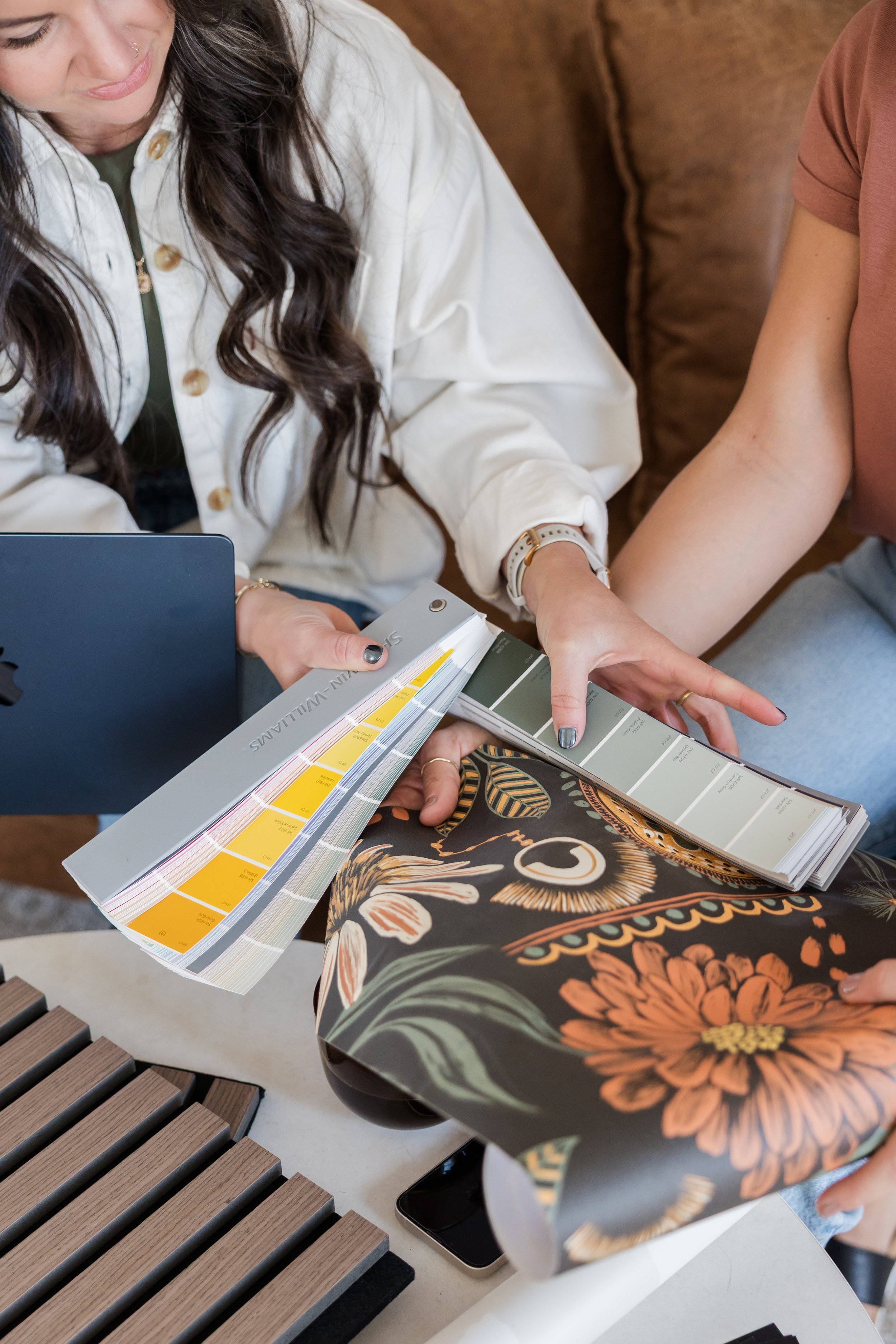 Two people examining color swatches and decorative wallpaper samples, likely in a design setting.