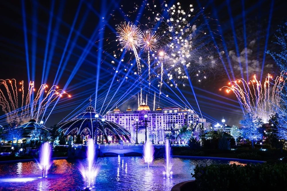 Universal Epic Universe view of the lake with fireworks bursting above and Helios Grand Hotel in the background