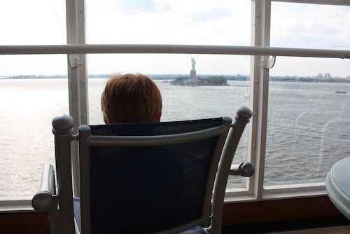 Young child sits in a chair gazing out a window with the Statue of Liberty in the distance
