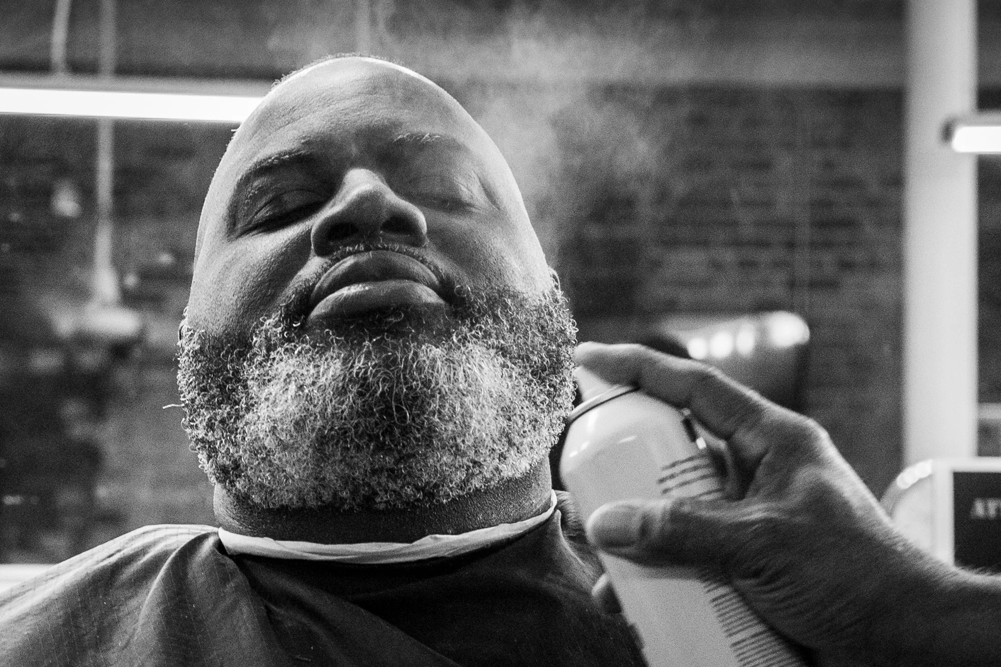 A customer receives the final touches on his beard after his hair is cut by barber Jeffery Warren on August 31, 2019. Warren, founder and owner of Signature Kutz, says he tries to make the Durham-based barber shop feel “homey, real comfortable. Like 
