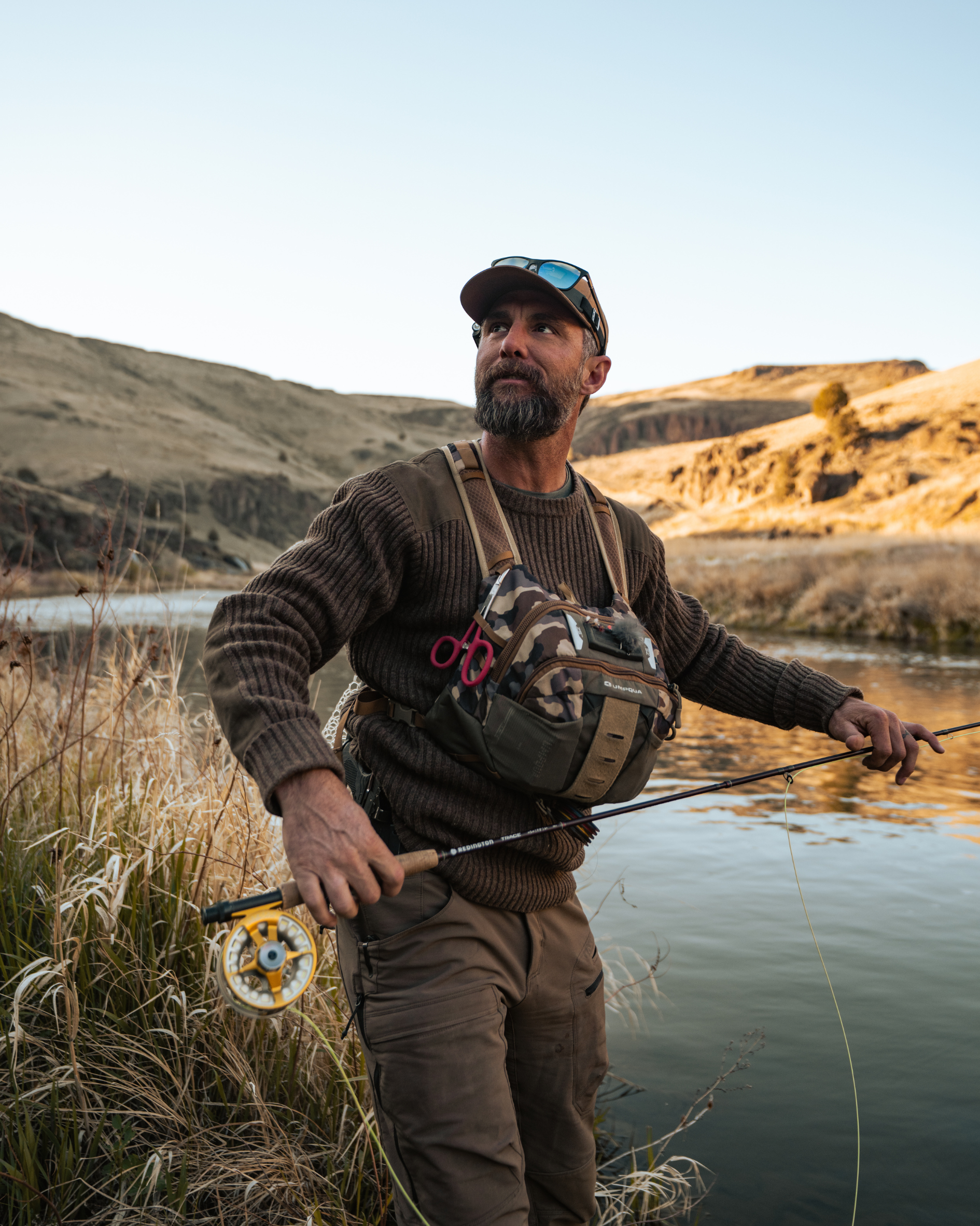 RYAN FLY FISHING ON THE RIVER IN ALL BROWN SURROUNDED BY WATER AND GOLDEN MOUNTAINS