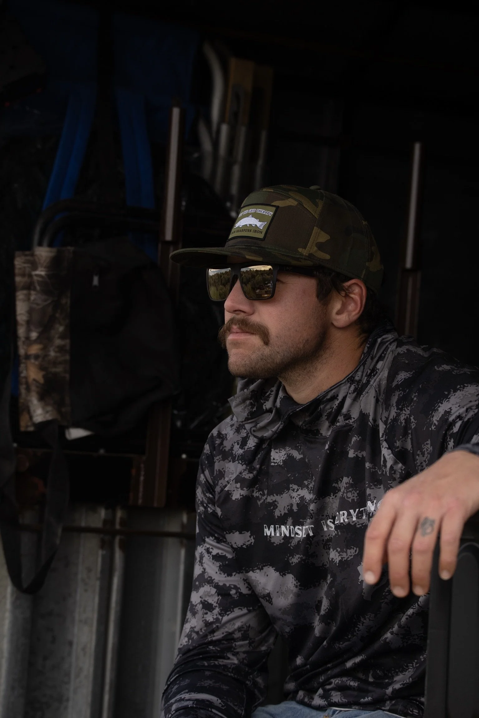 BRET IN CAMO LOOKING OUT AT THE LANDSCAPE WEARING CAMO HAT AND CAMO SHIRT WITH SUNGLASSES