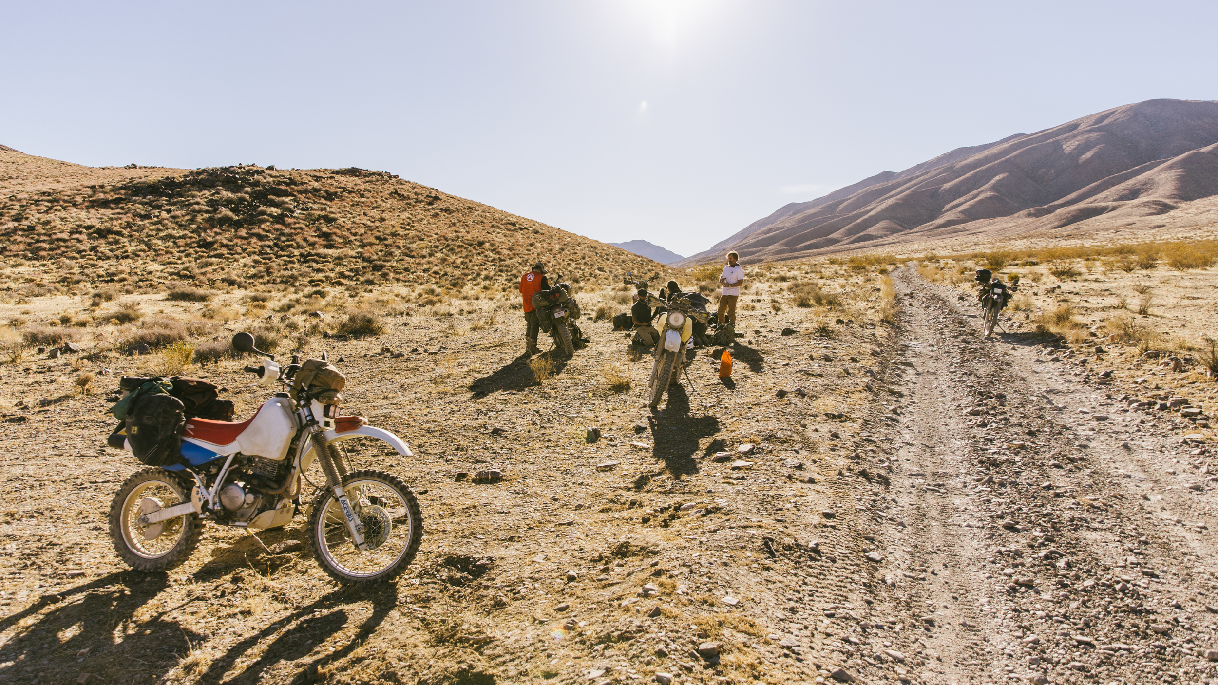 dirtbikes on the side of a dirt road with the riders taking a break in the hot baja sun 