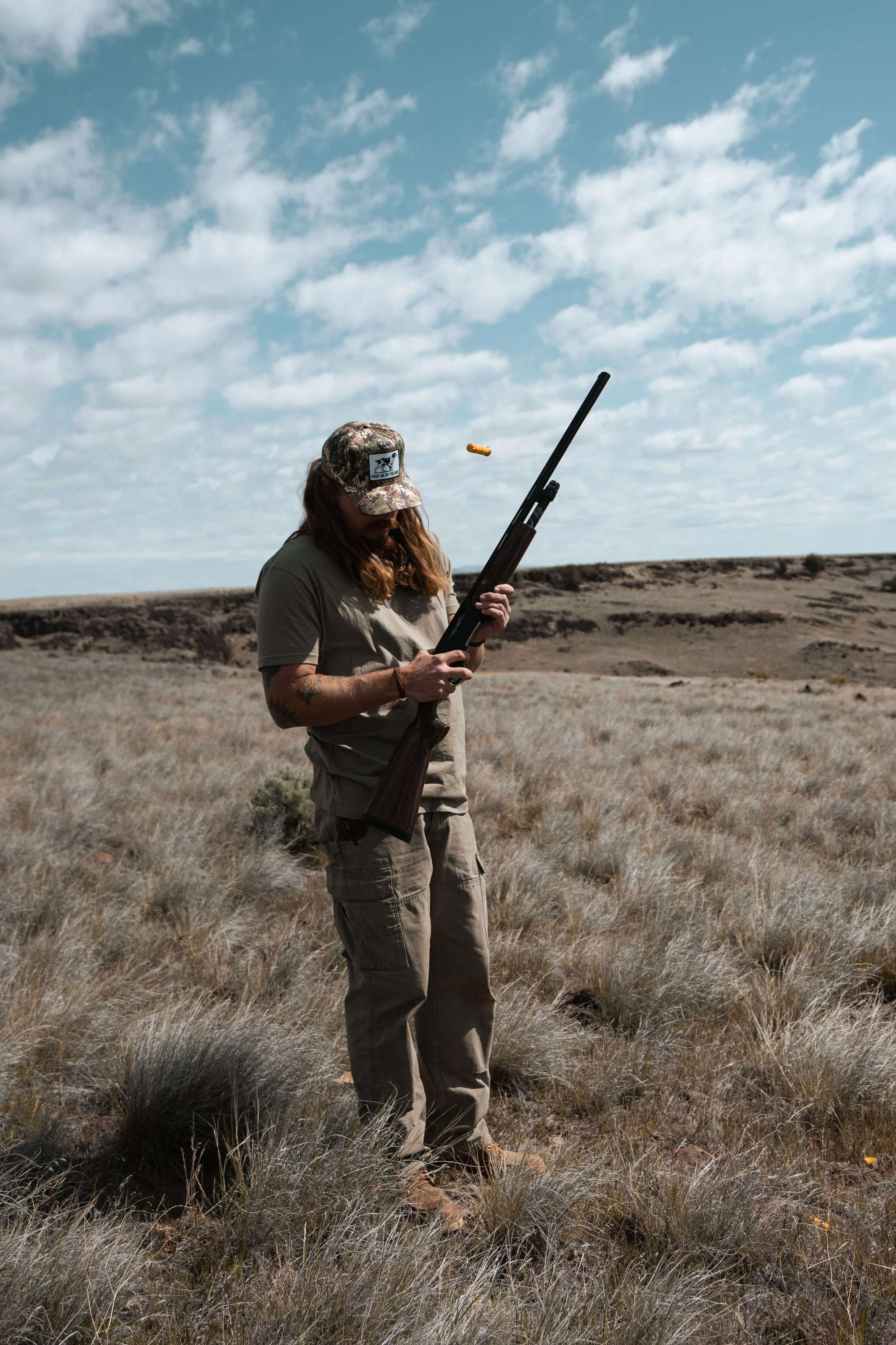 A man standing in a grass field shooting a riffle wearing all army green