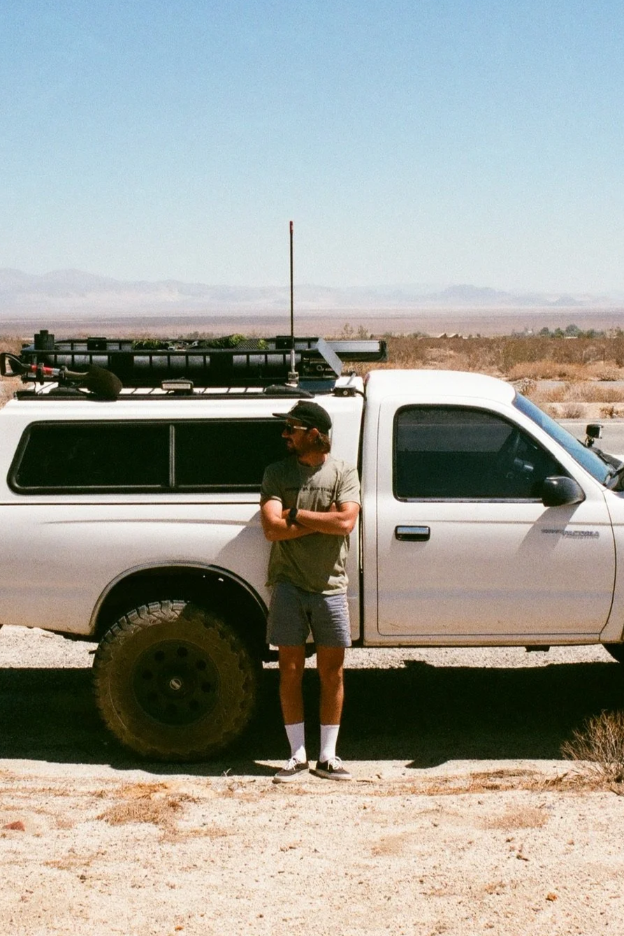 ADRIAN STANDING AGAINST HIS WHITE TOYOTA TACOMA WITH HANDS FOLDED LOOKING OFF IN TO THE DISTANCE