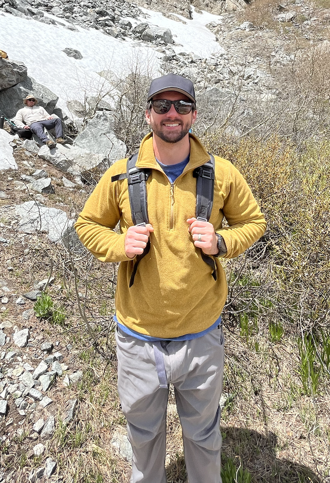 branden standing on the side of a mountain in a yellow sweatshirt and backpack smiling while on a hike
