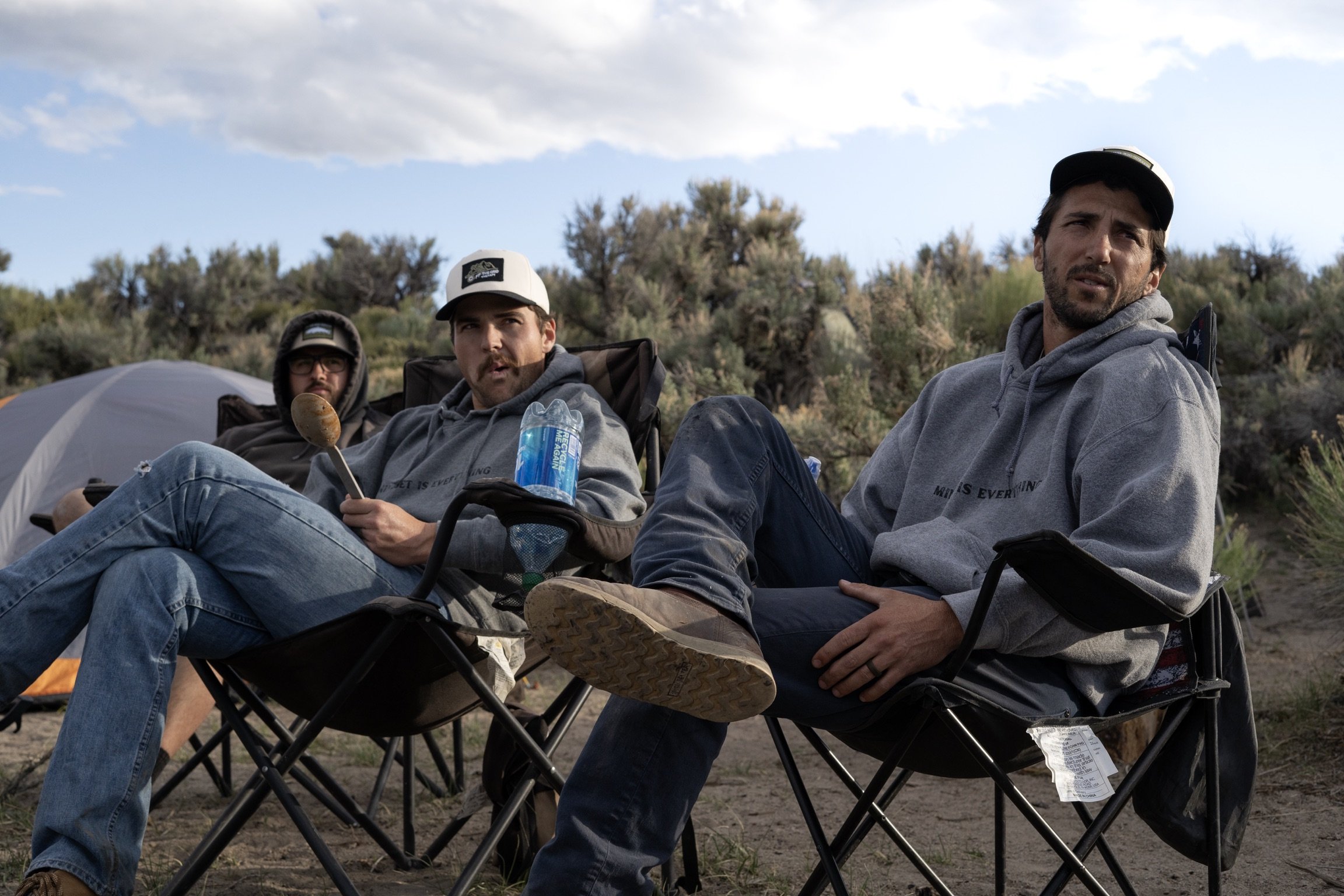 SHANE ELIAS CALLES SITTING IN A CHAIR WEARING A GREY HOODIE AND BASEBALL HAT
