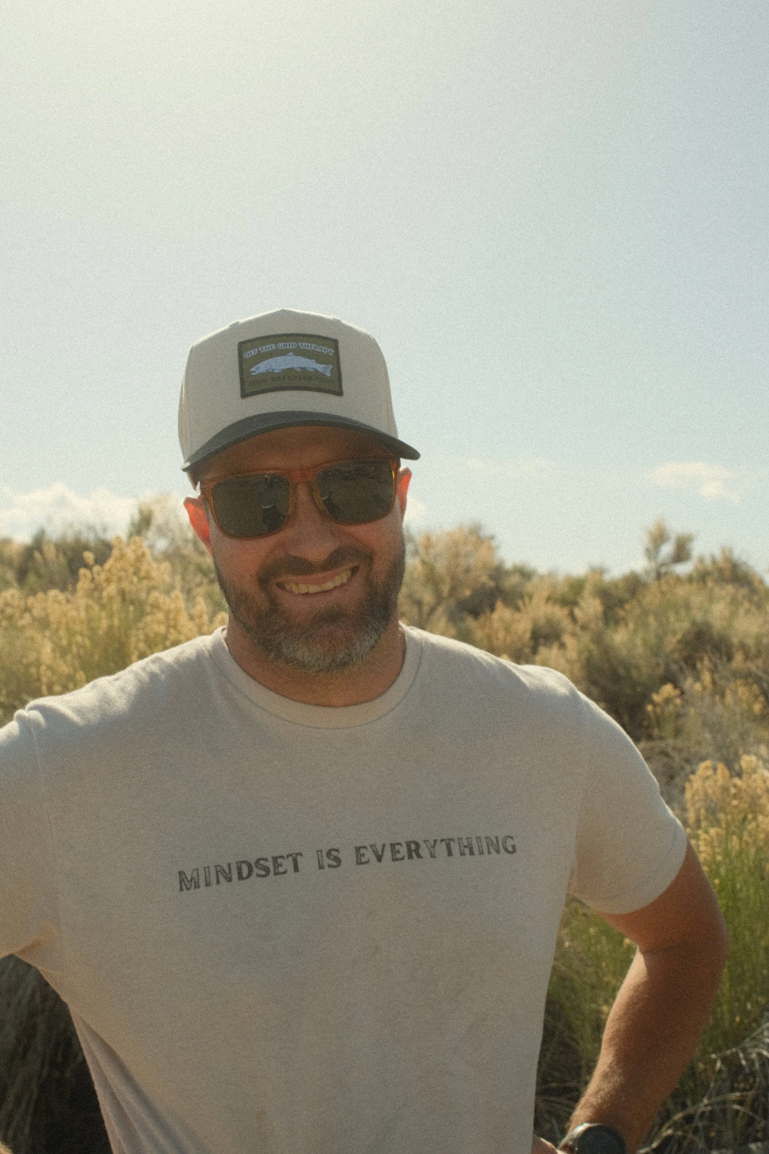 ELLIOTT SMILING IN A OFF THE GRYD HAT WITH A WHITE SHIRT THAT SAYS MINDSET IS EVERYTHING
