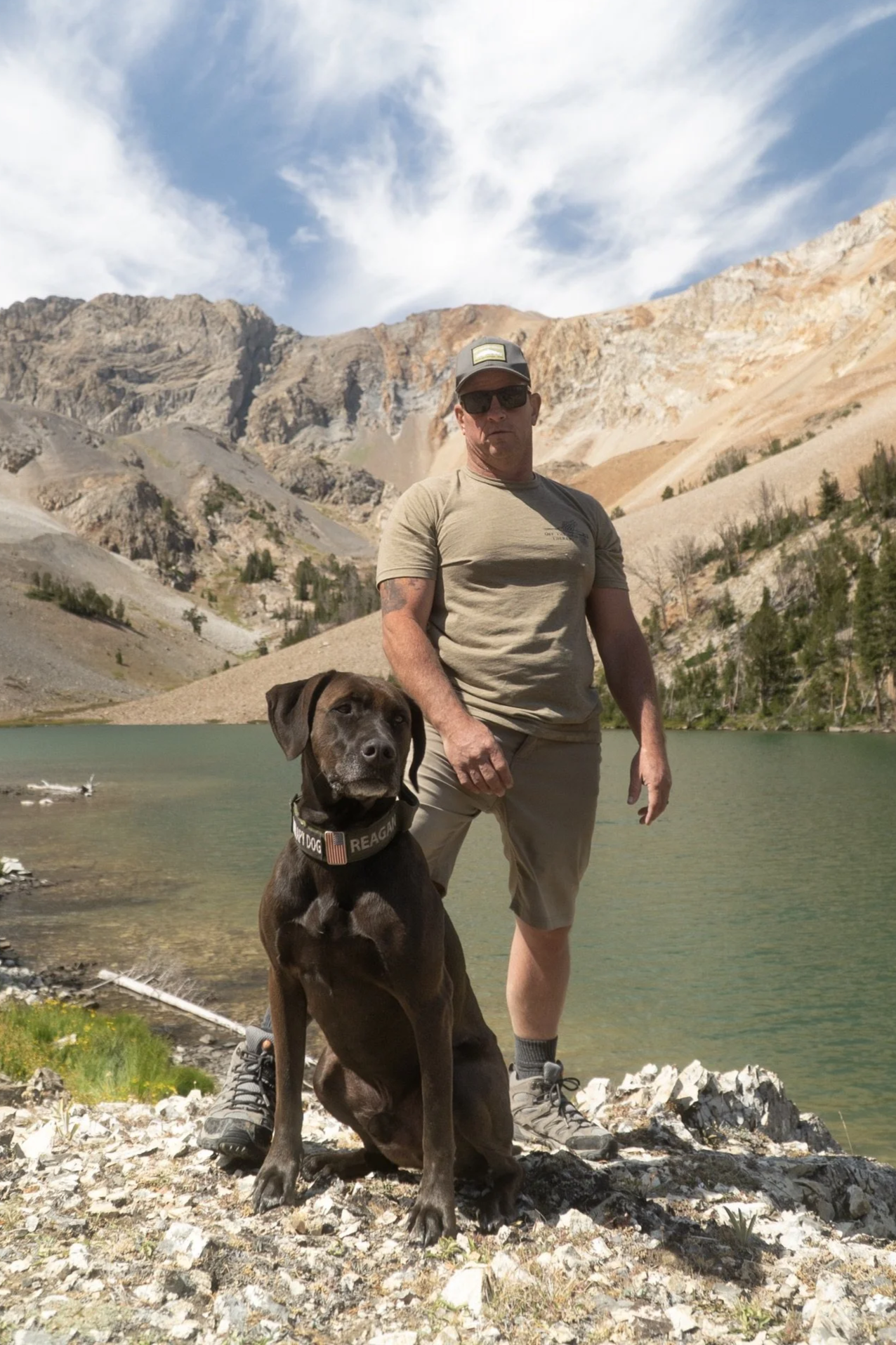 CHRIS LOGAN AND DOG REGAN STANDING NEXT TO LAKE AND SMALL MOUNTAINS