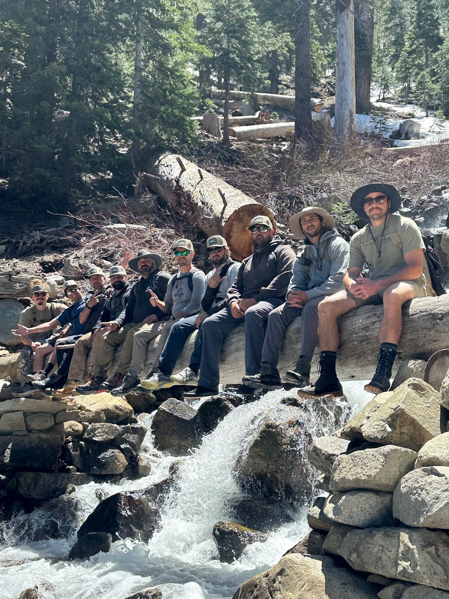LOTS OF GUYS SITTING ON A LOG OVER A WATERFALL SMILING AT THE CAMERA
