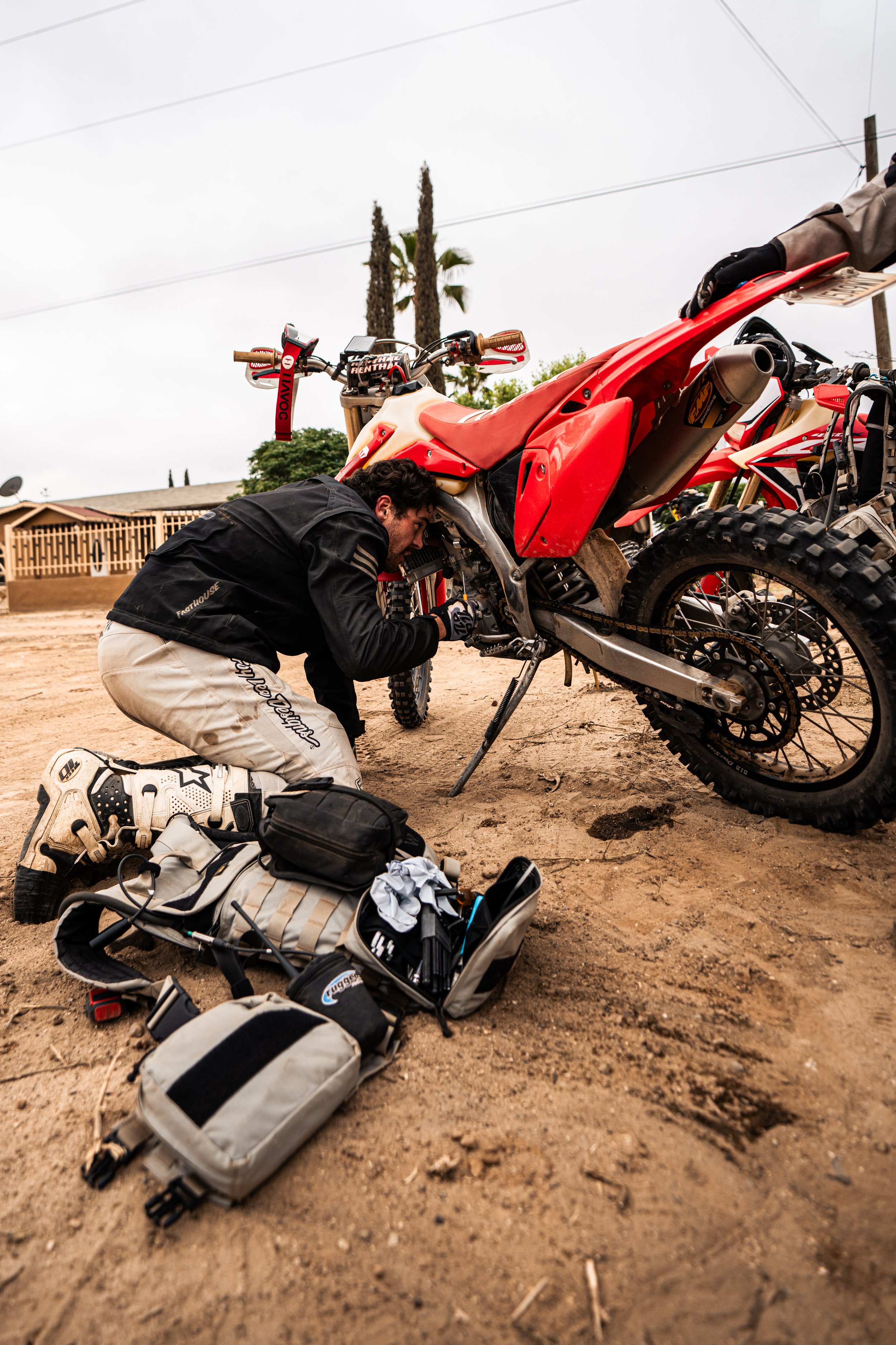 dirtbikes on the side of a dirt road with the riders taking a break in the hot baja sun working on bike