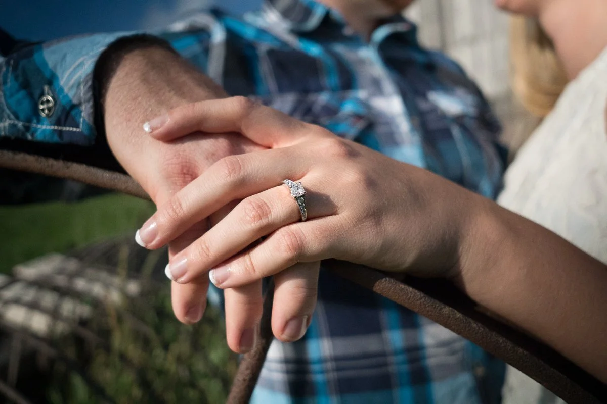 Close-up of a couple holding hands, with the woman wearing an engagement ring, during a romantic moment.