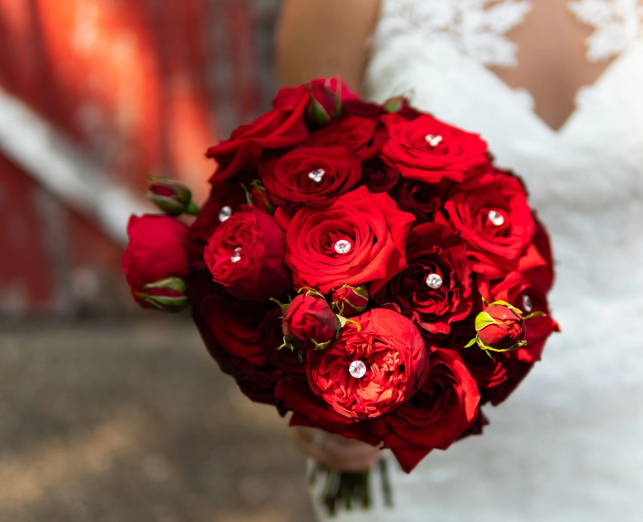 Close-up of a bridal bouquet with red roses decorated with small rhinestones, held by a bride in a white dress