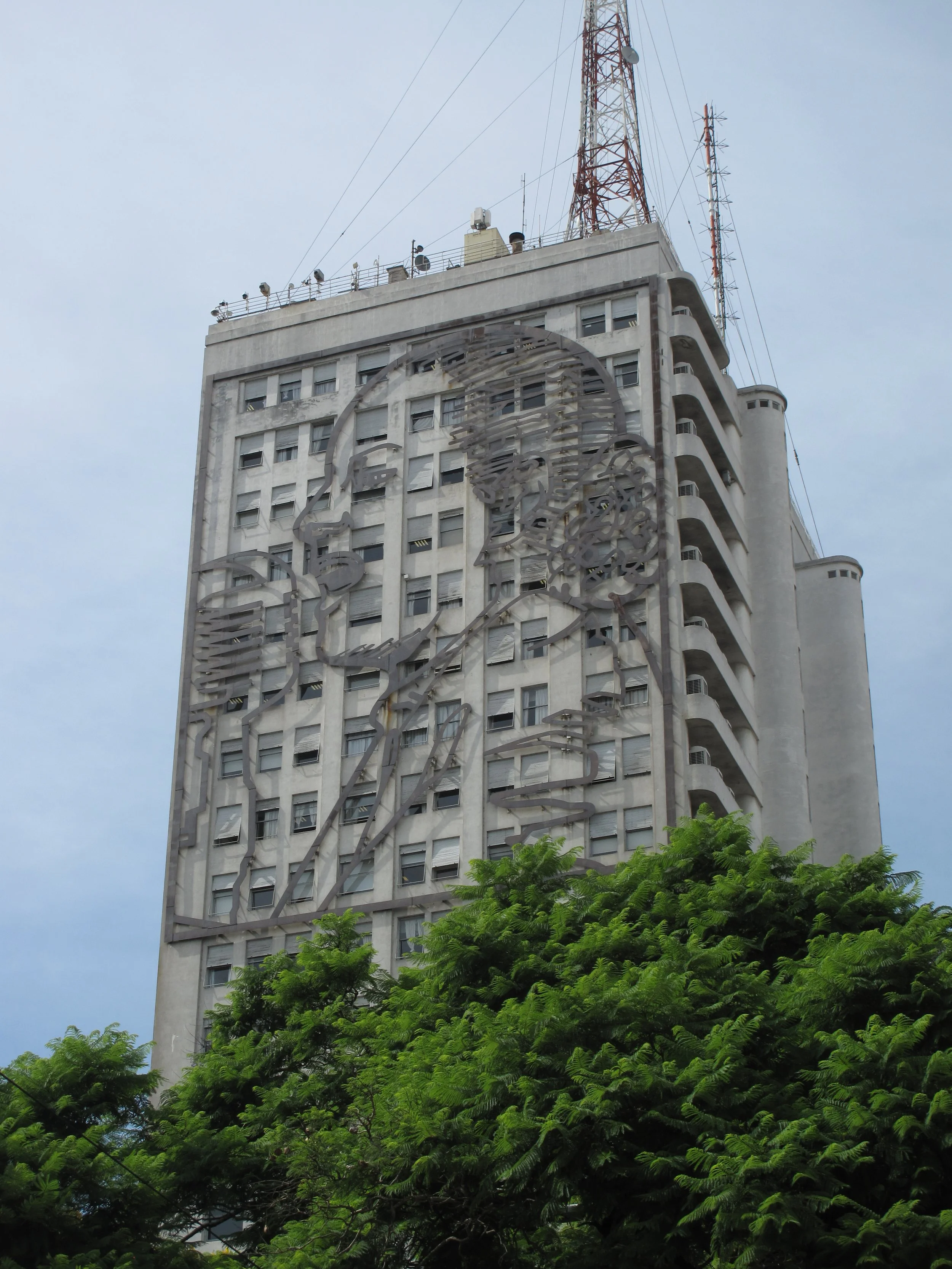 Tall building with a mural of a man's profile surrounded by trees.