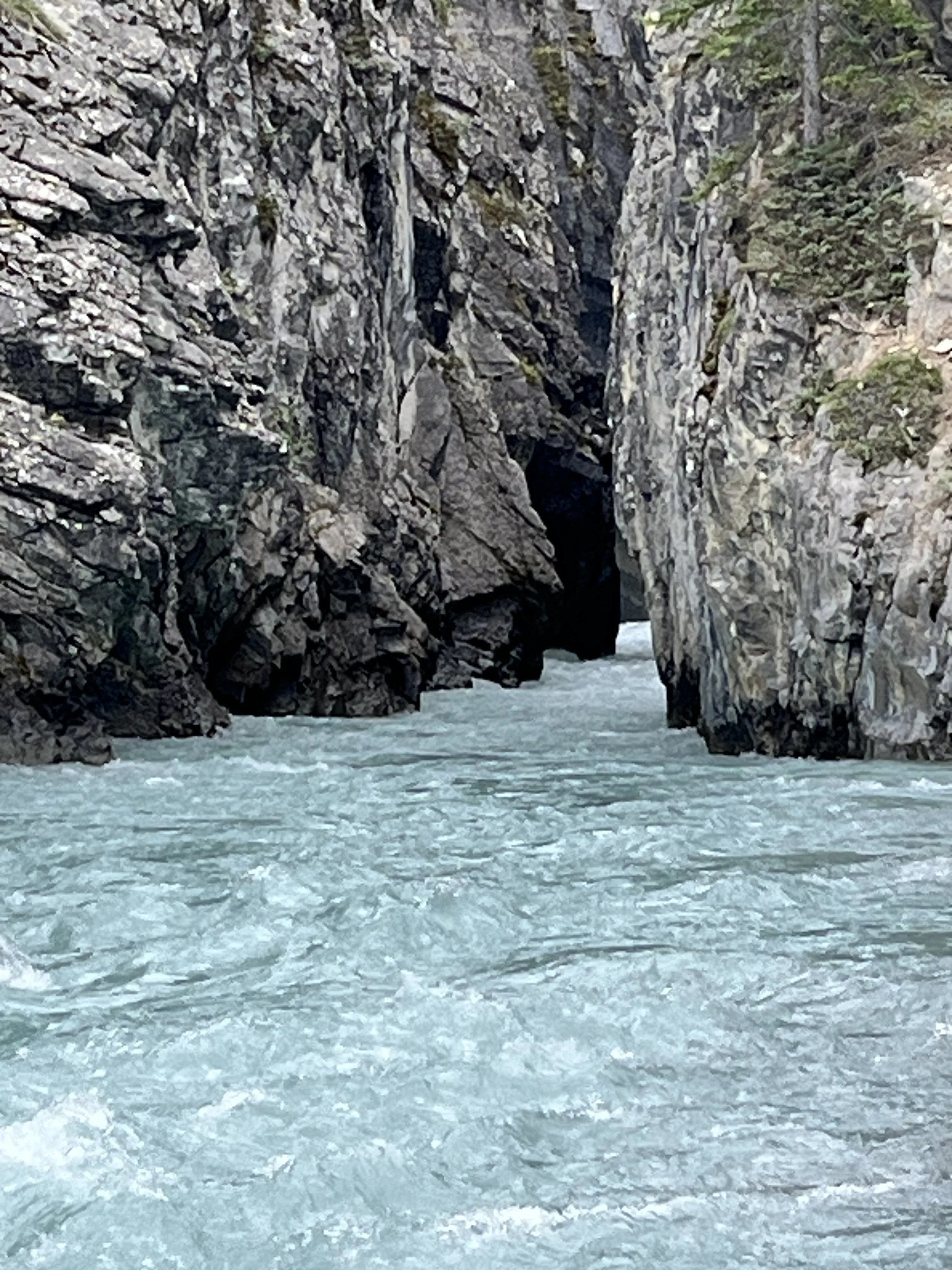 A narrow section of a river with light turquoise water flowing between high rocky canyon walls.