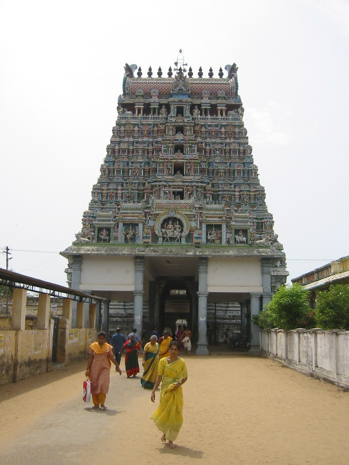 People walking towards a colorful Hindu temple with intricate carvings and sculptures in Tamil Nadu, India.