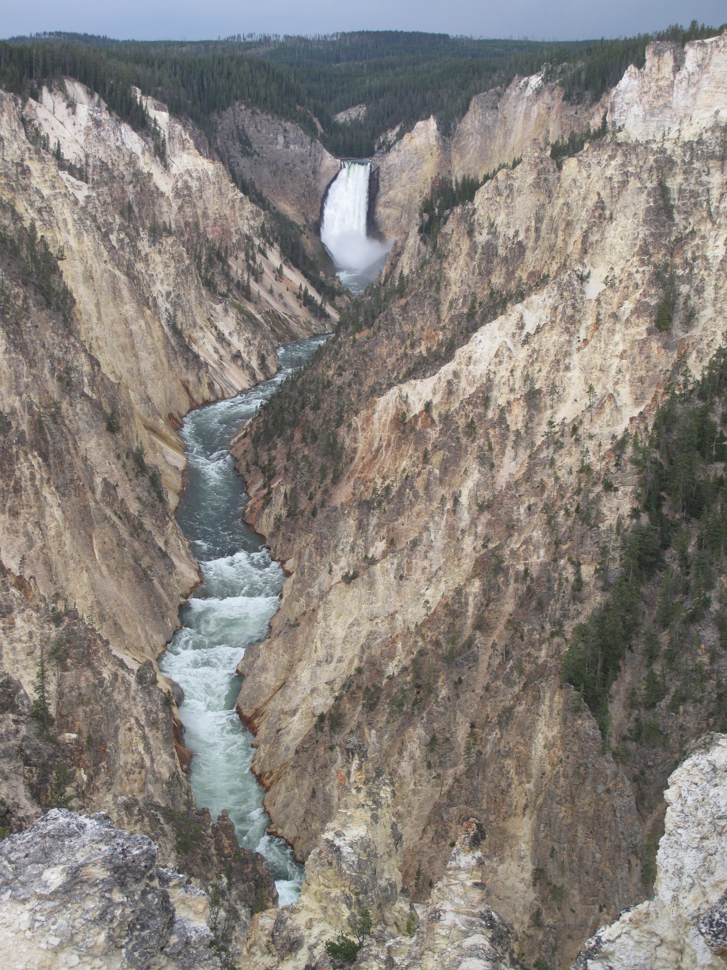 A valley with a river flowing through it, surrounded by steep rocky cliffs, with a waterfall in the background, possibly in a national park area.