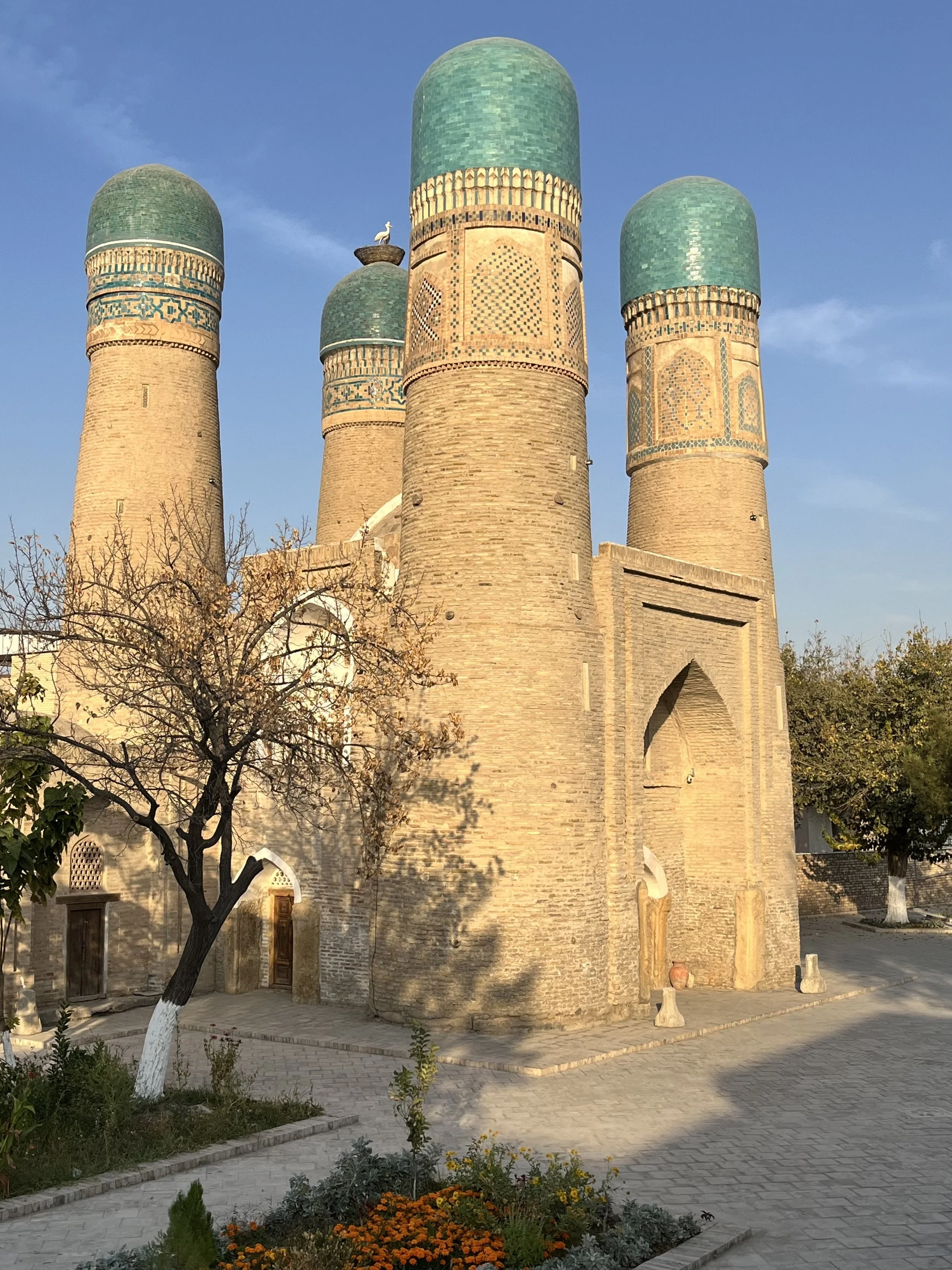 Historic building with four tall cylindrical towers topped with turquoise domes, decorated with intricate patterns, under a clear blue sky.