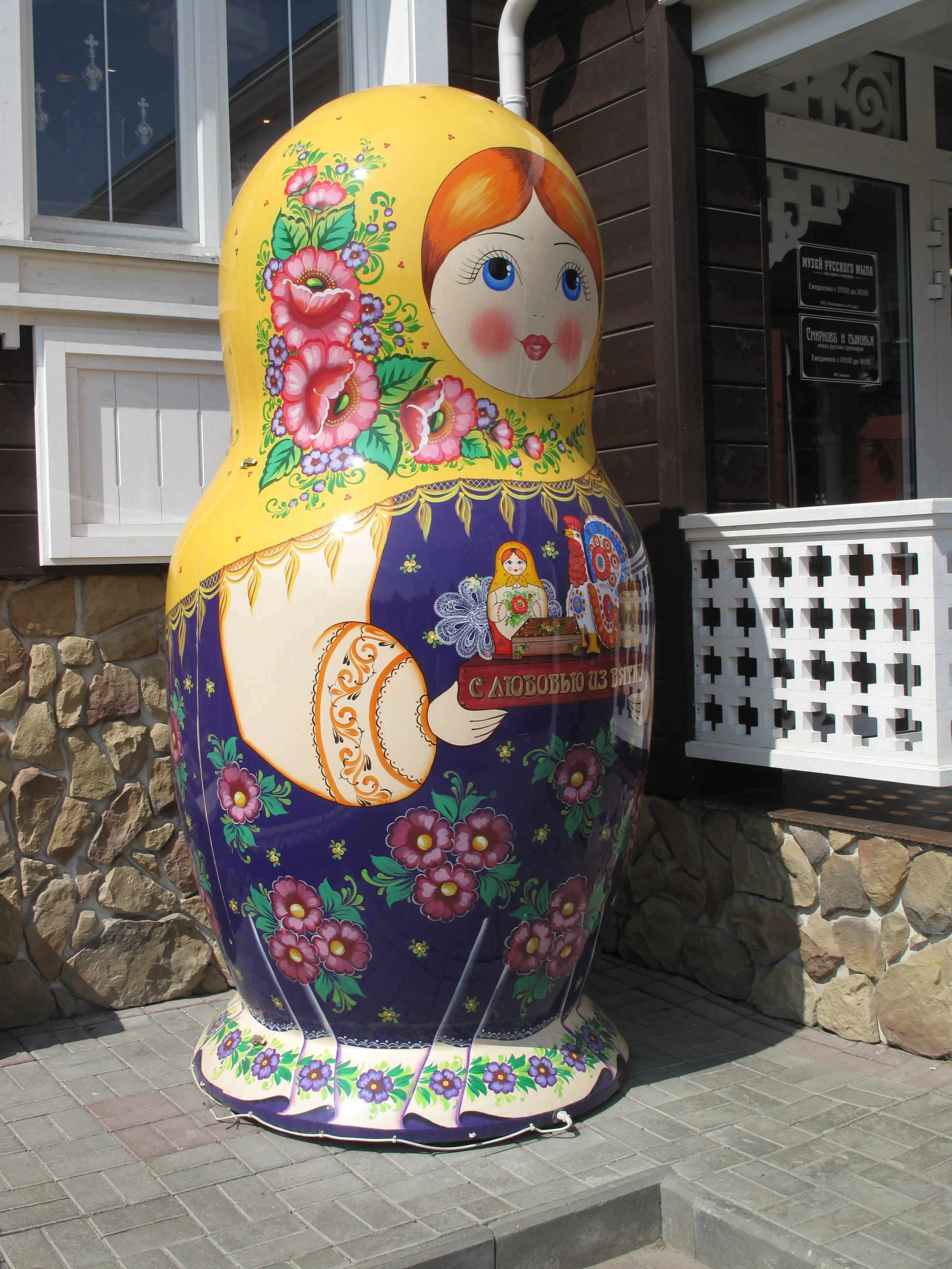 Colorful painted matryoshka doll sculpture outside a building with stone and wood exterior.