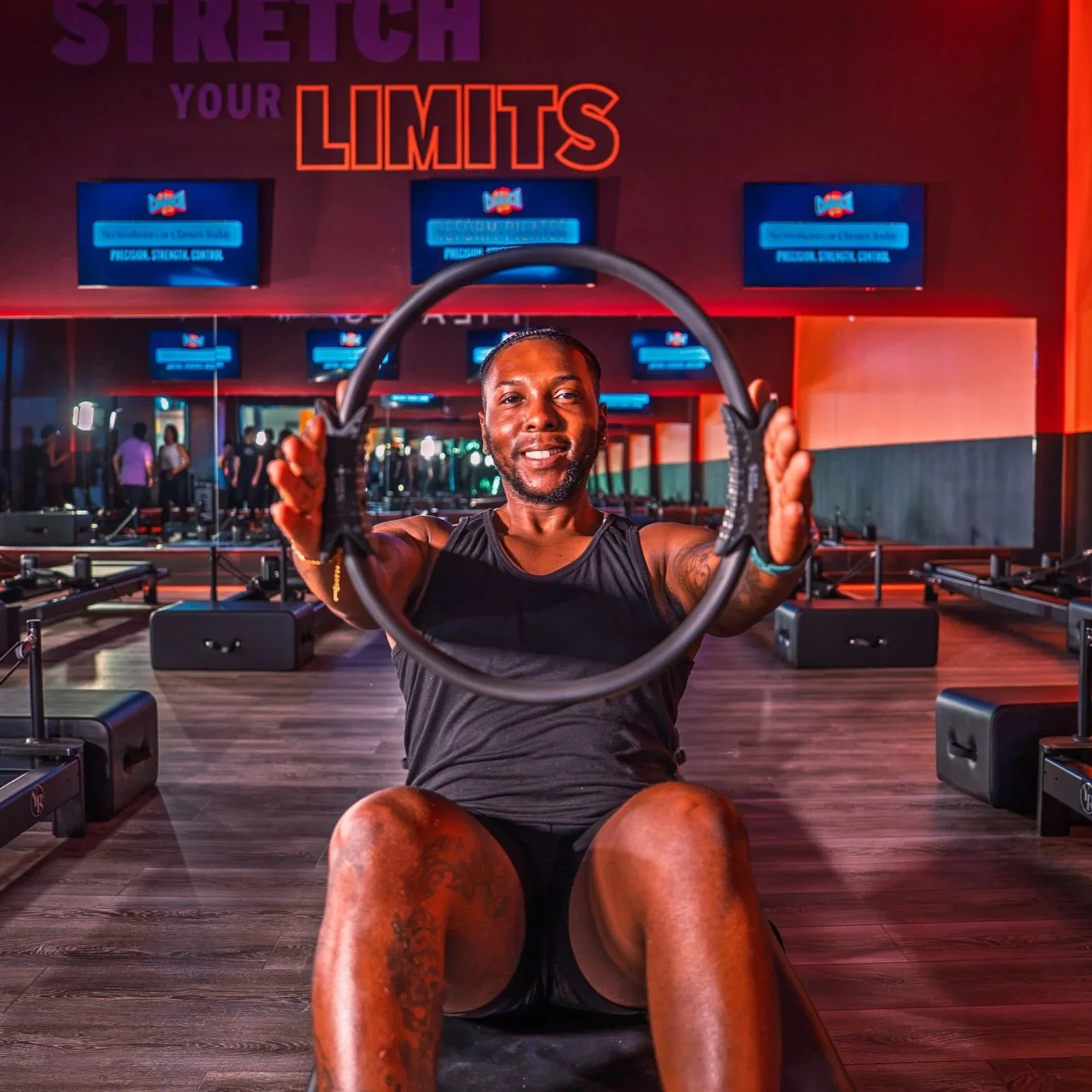 A man doing an ab exercise in a gym, holding a fitness ring in front of him, with an encouraging sign on the wall behind him that says 'Stretch Your Limits'.