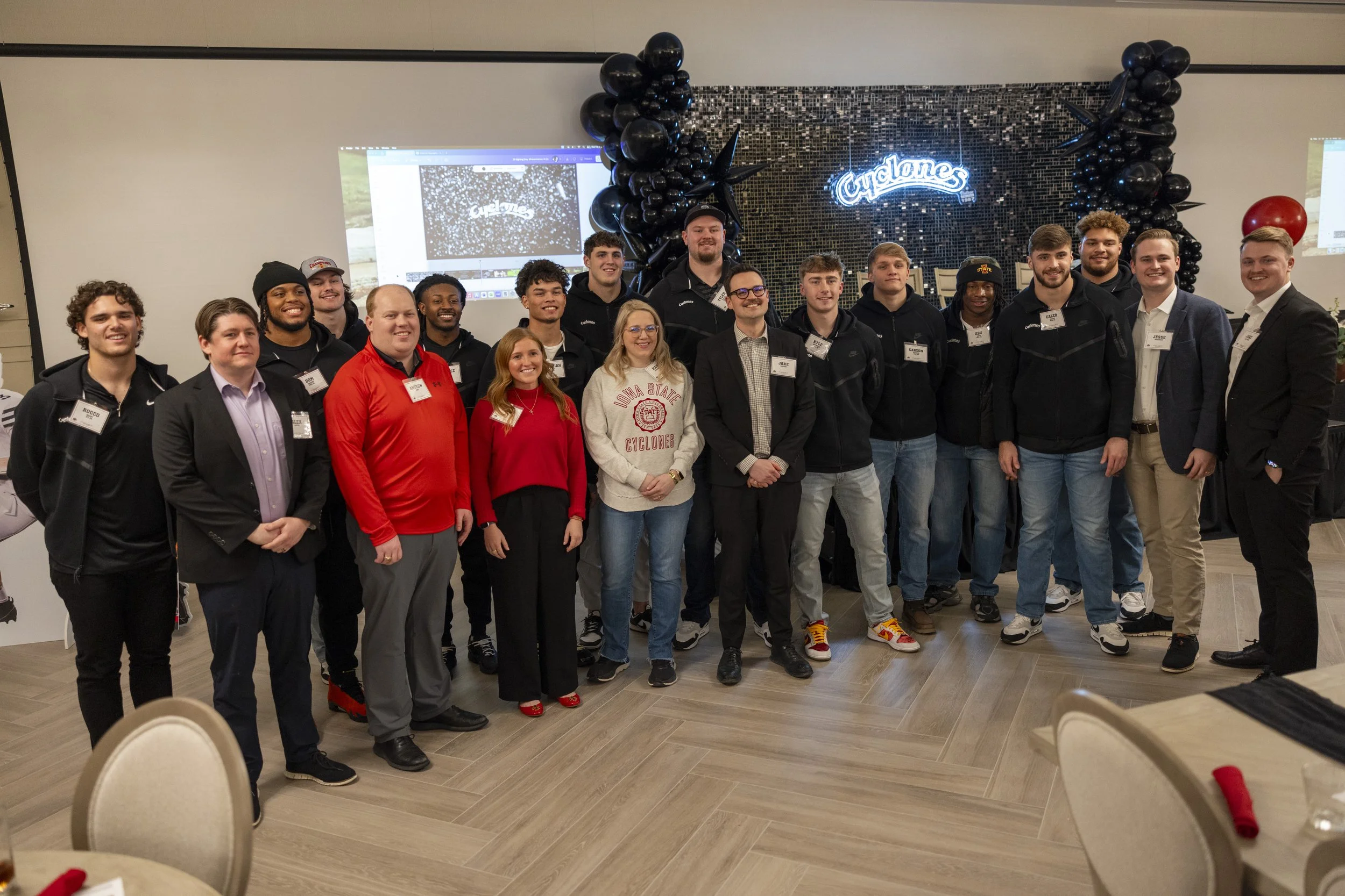 Group of people posing in a room with "Cyclones" sign and black balloon decorations