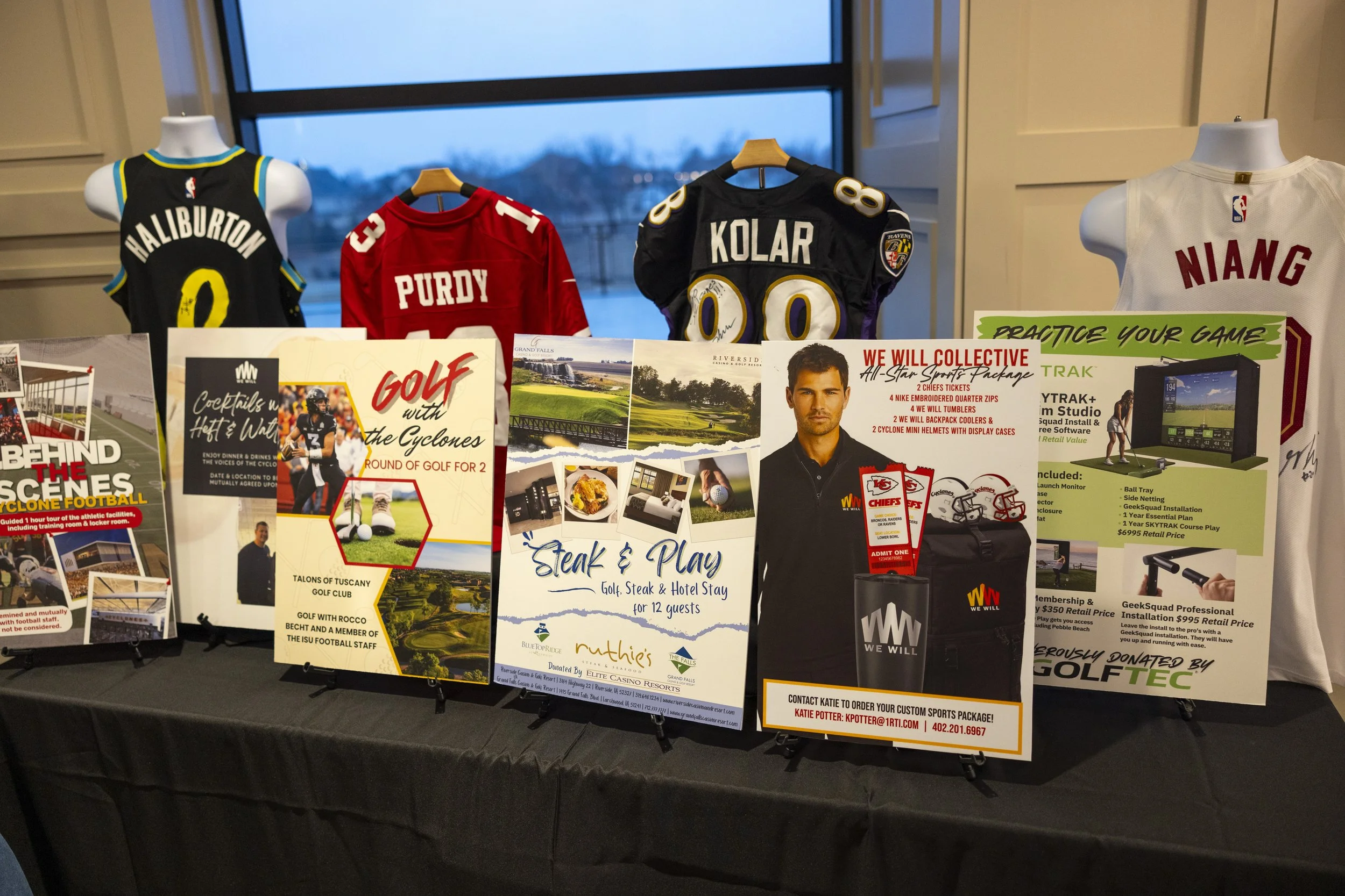 Mannequins displaying sports jerseys and advertising posters in a room. Jerseys include names "Haliburton," "Purdy," "Kolar," and "Niang." Posters promote events and products like "Golf with the Cyclones," "Steak & Play," and packages from "We Will C
