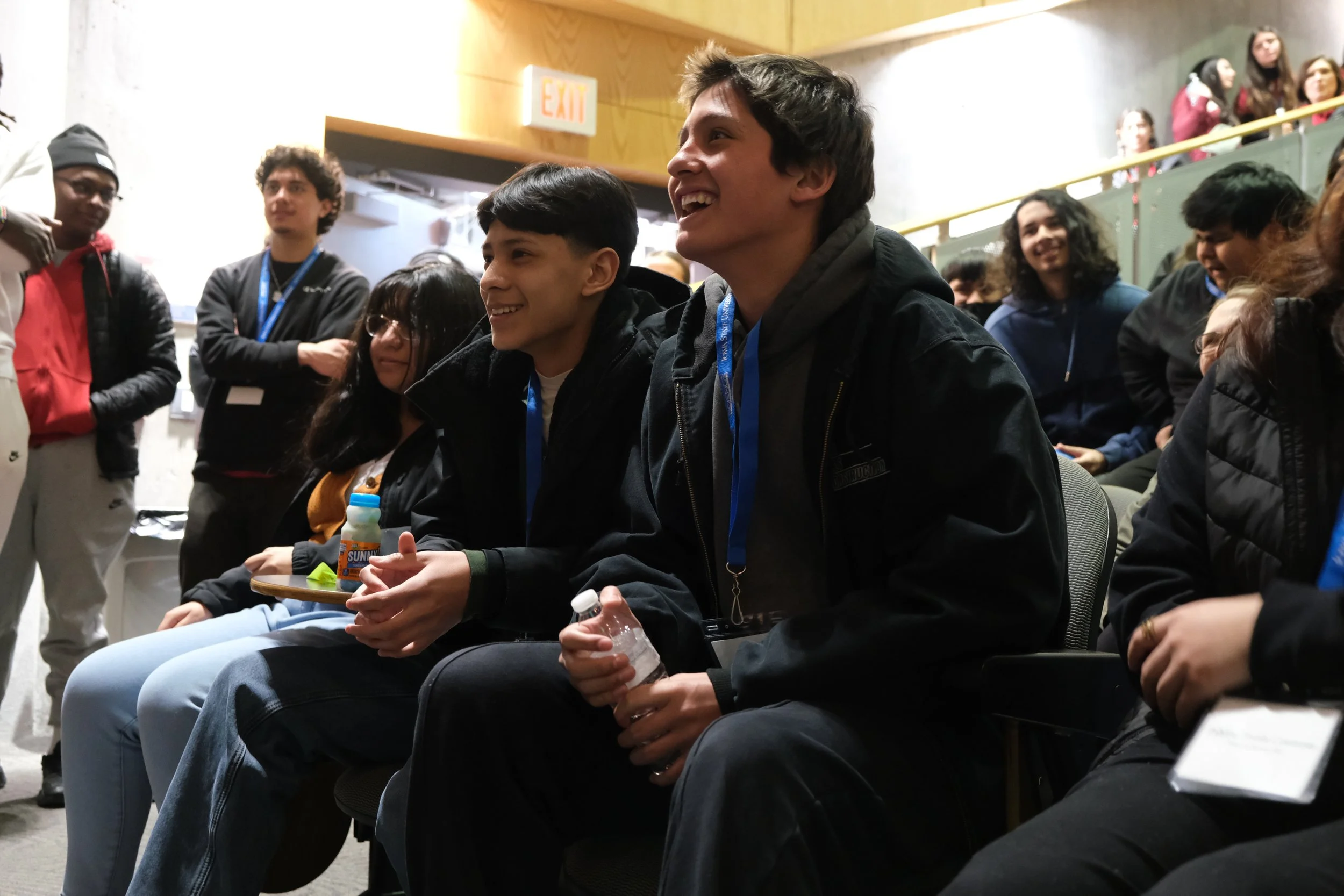 Group of young people smiling and sitting in a classroom setting.