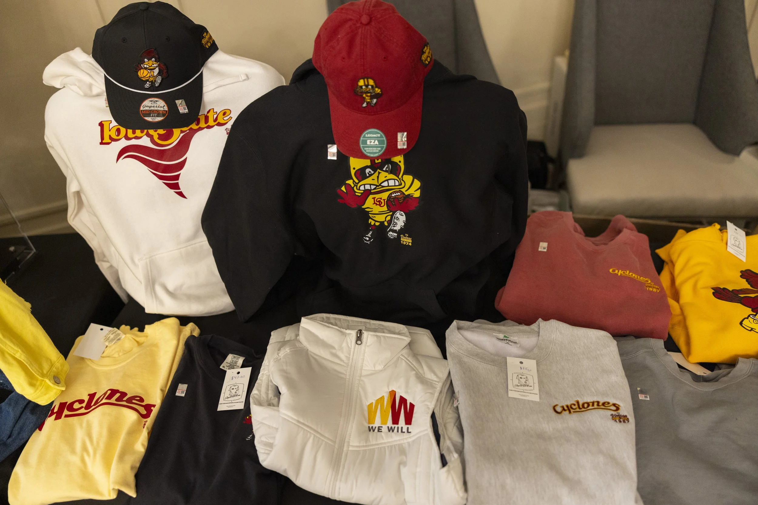 Assorted Iowa State Cyclones apparel including hoodies, T-shirts, and hats displayed on a table.