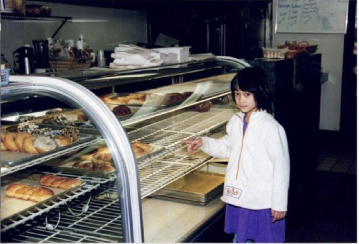 A young Dorothy chow pointing to a pastry inside a pastry and donut display case