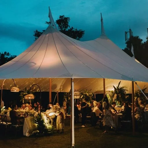 An aerial shot of a tent in the middle of a field at Komune Resort in Bali. The tent is white and has a peaked roof. It is surrounded by trees and the resort's buildings.