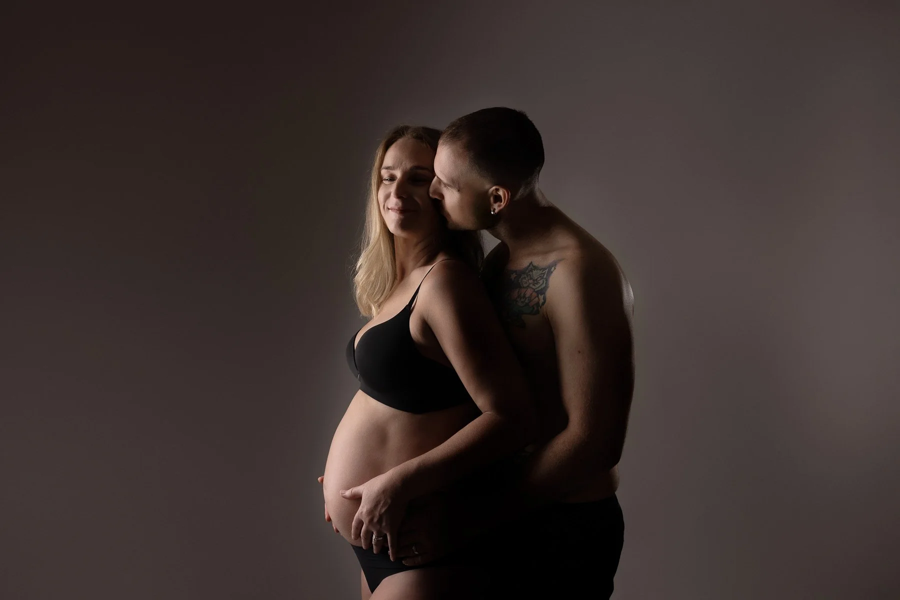 couple hugging touching the pregnant belly, wearing just underwears on a grey backdrop