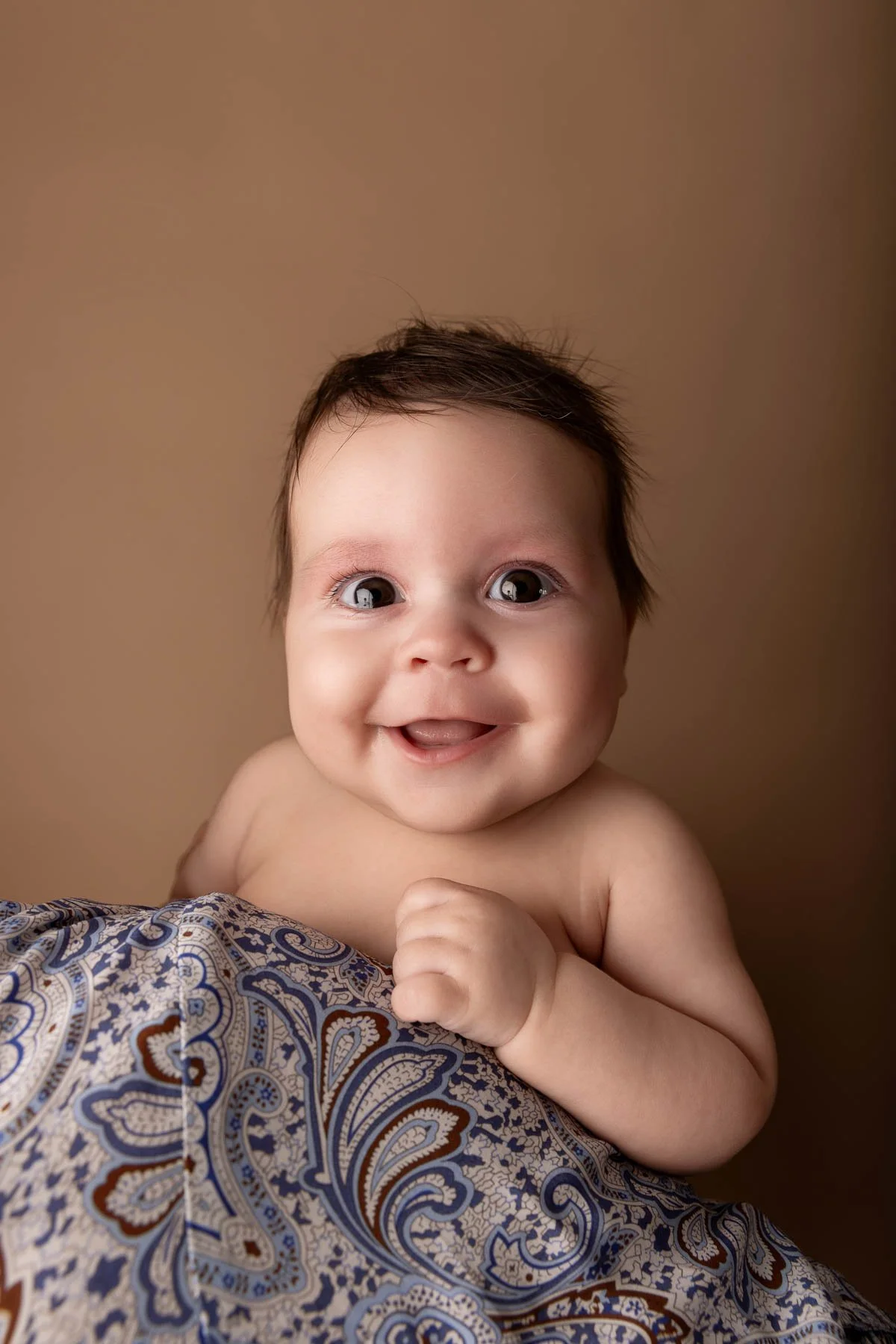 Smiling baby with paisley patterned fabric, brown background