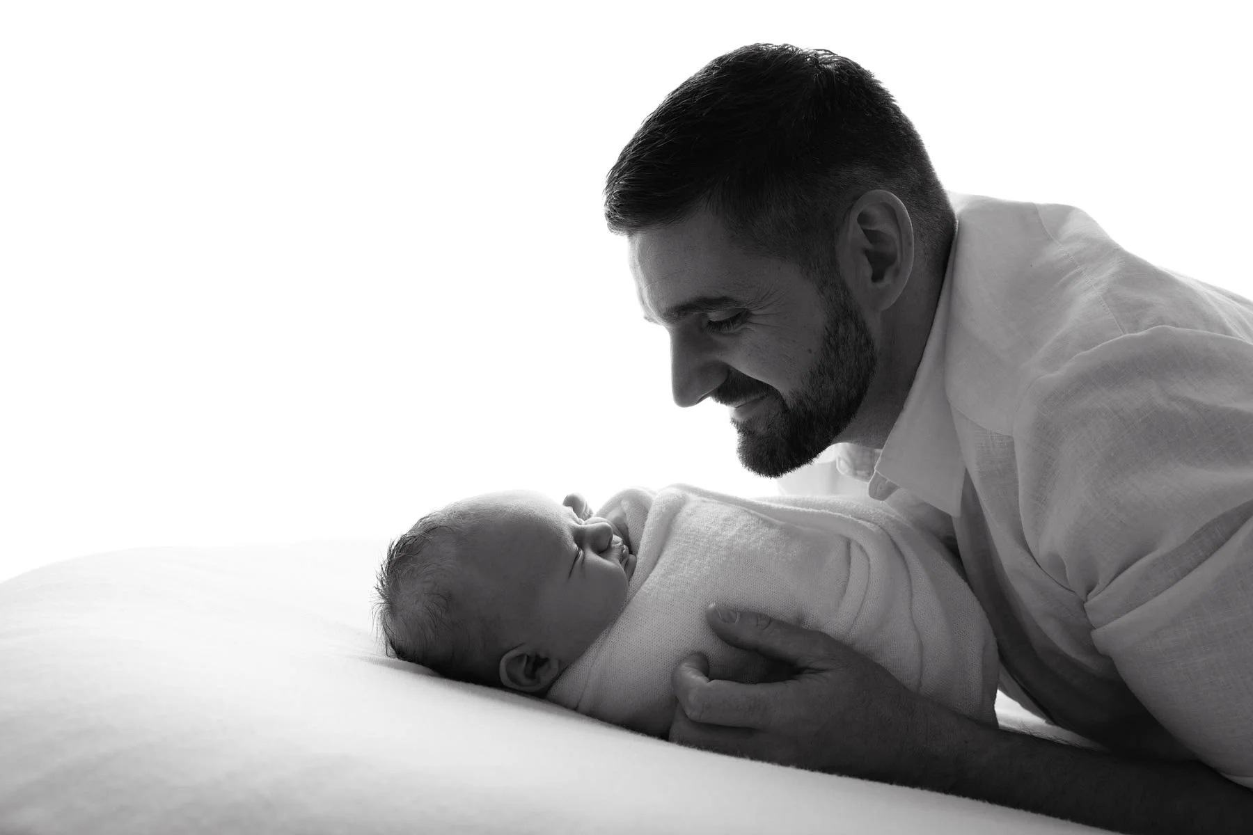 dad leaning over his baby smiling, in black and white