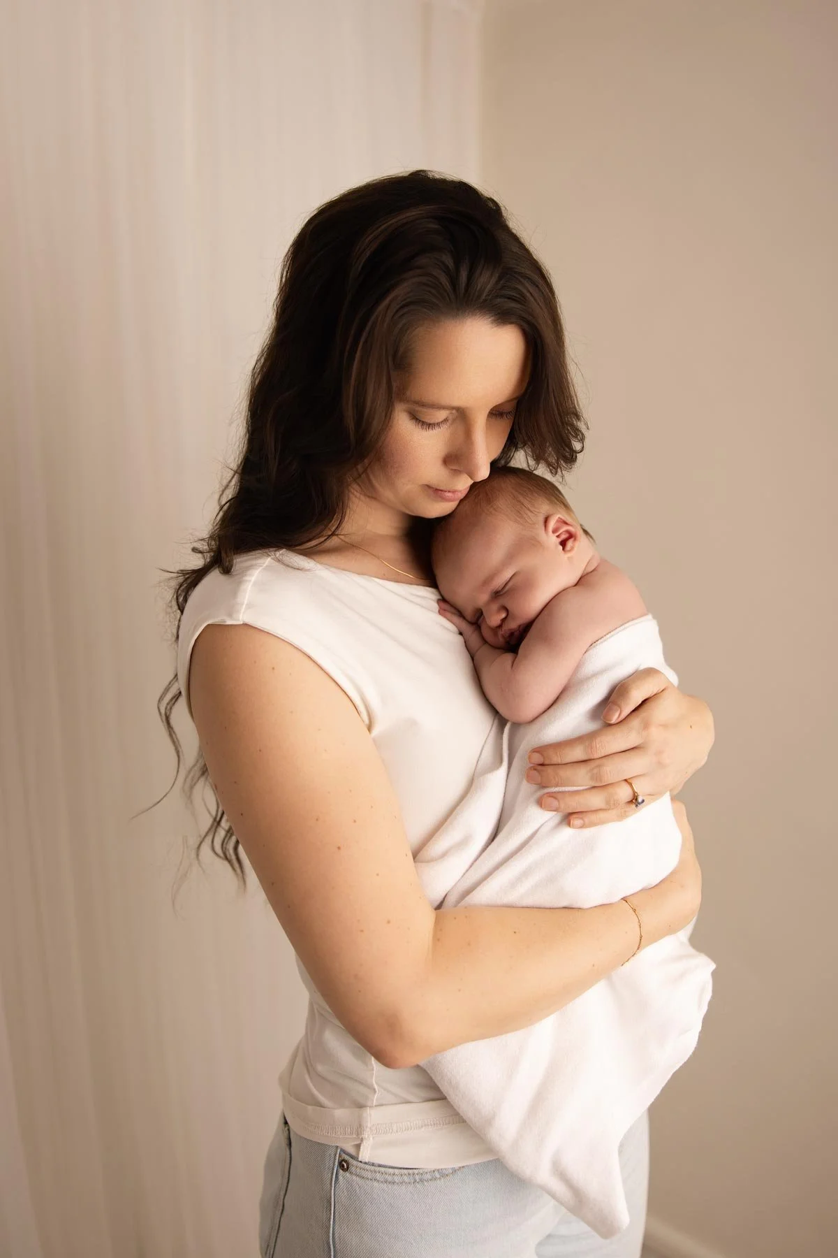 Mother holding a sleeping baby wrapped in a white blanket.