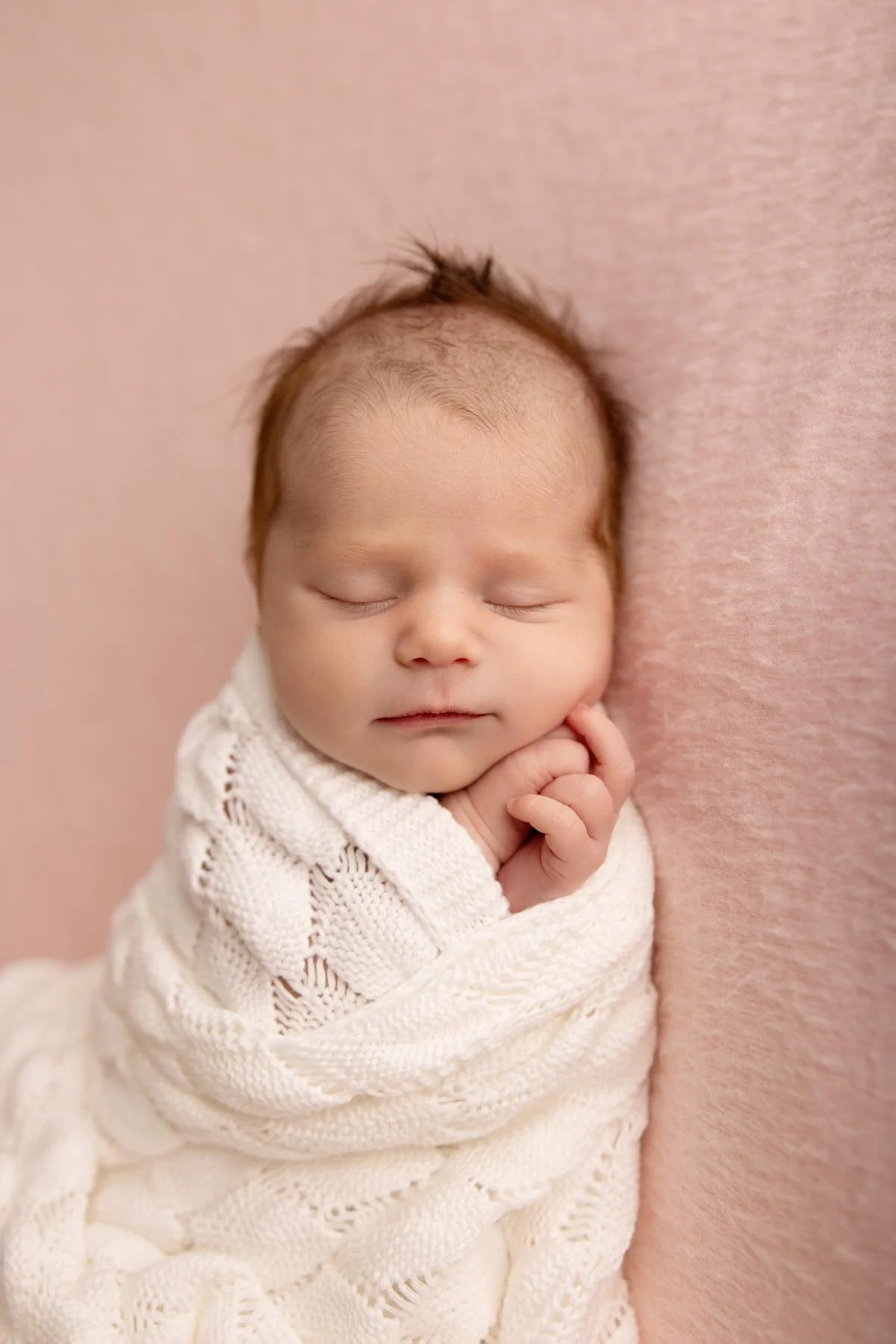 baby girl wrapped in a lace wrap, on a pink blanket