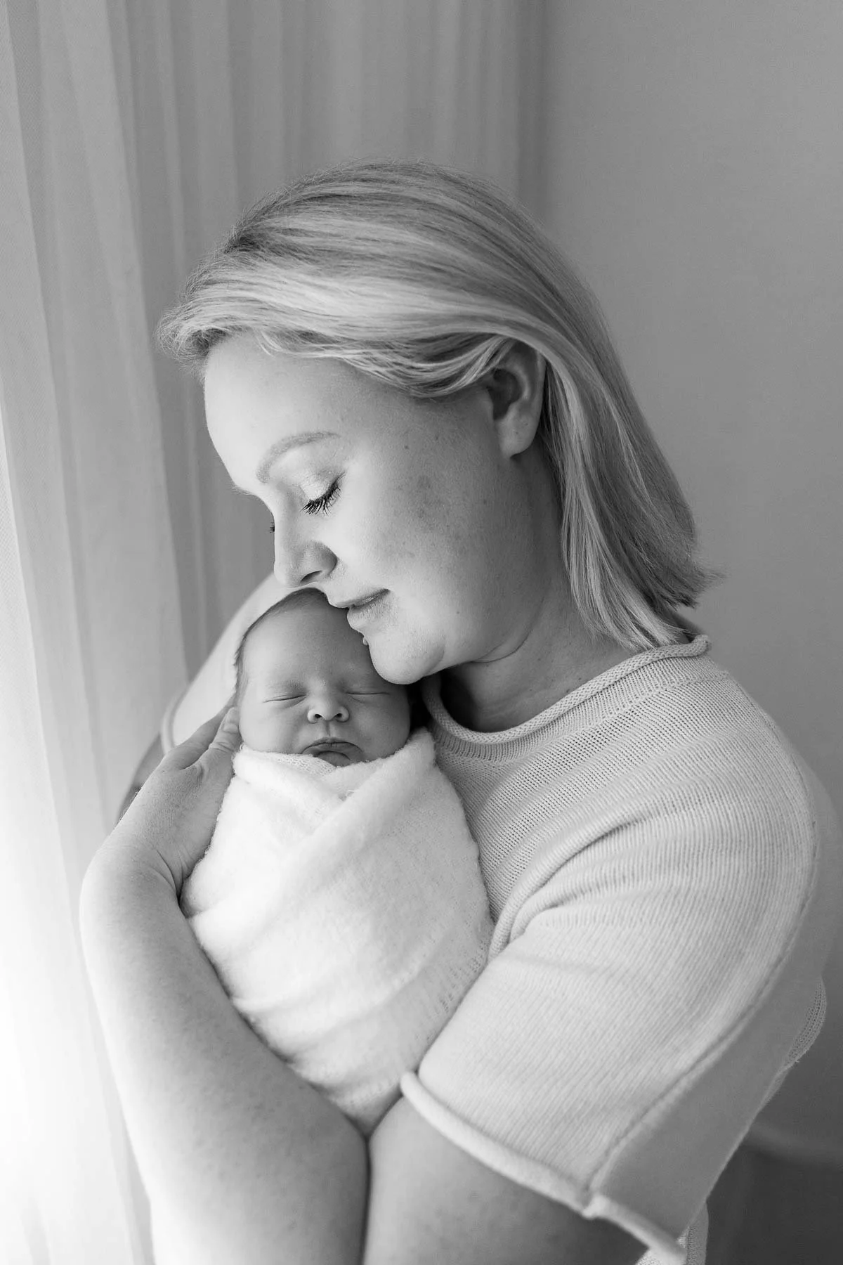 Mother holding a sleeping baby wrapped in a white blanket.