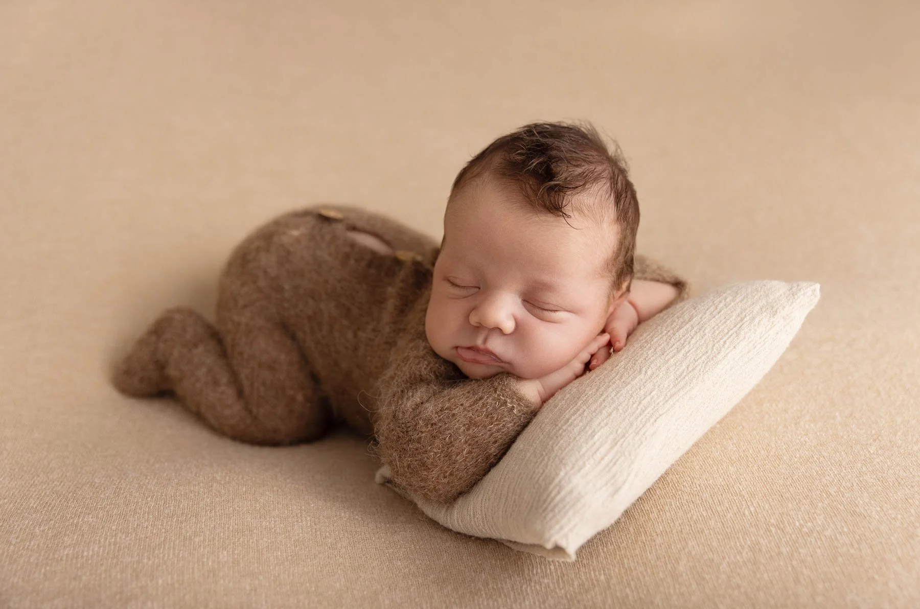 Newborn baby laying on his tummy with a little pillow wearing a knitted brown outfit