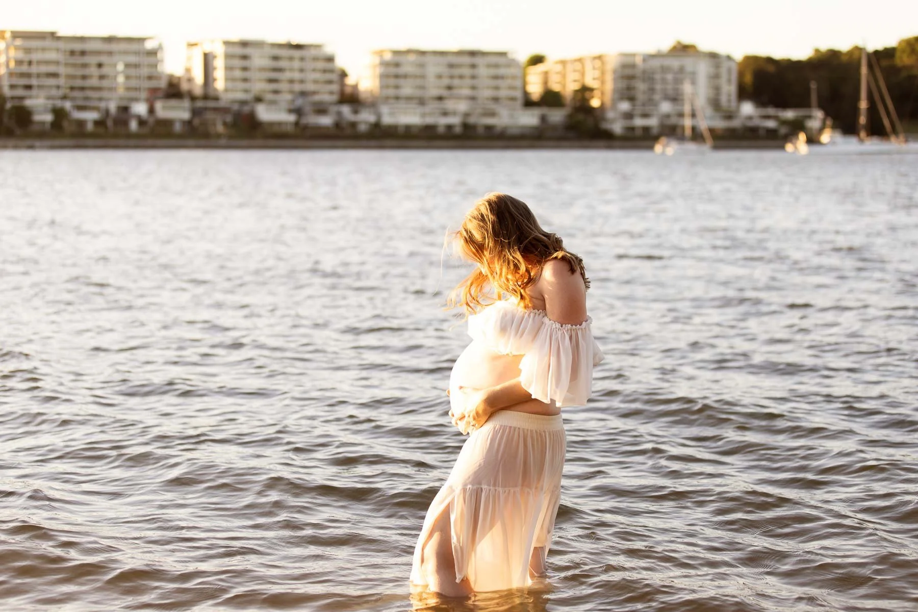Pregnant woman in white dress in the water at sunset North Shore Maternity photographer