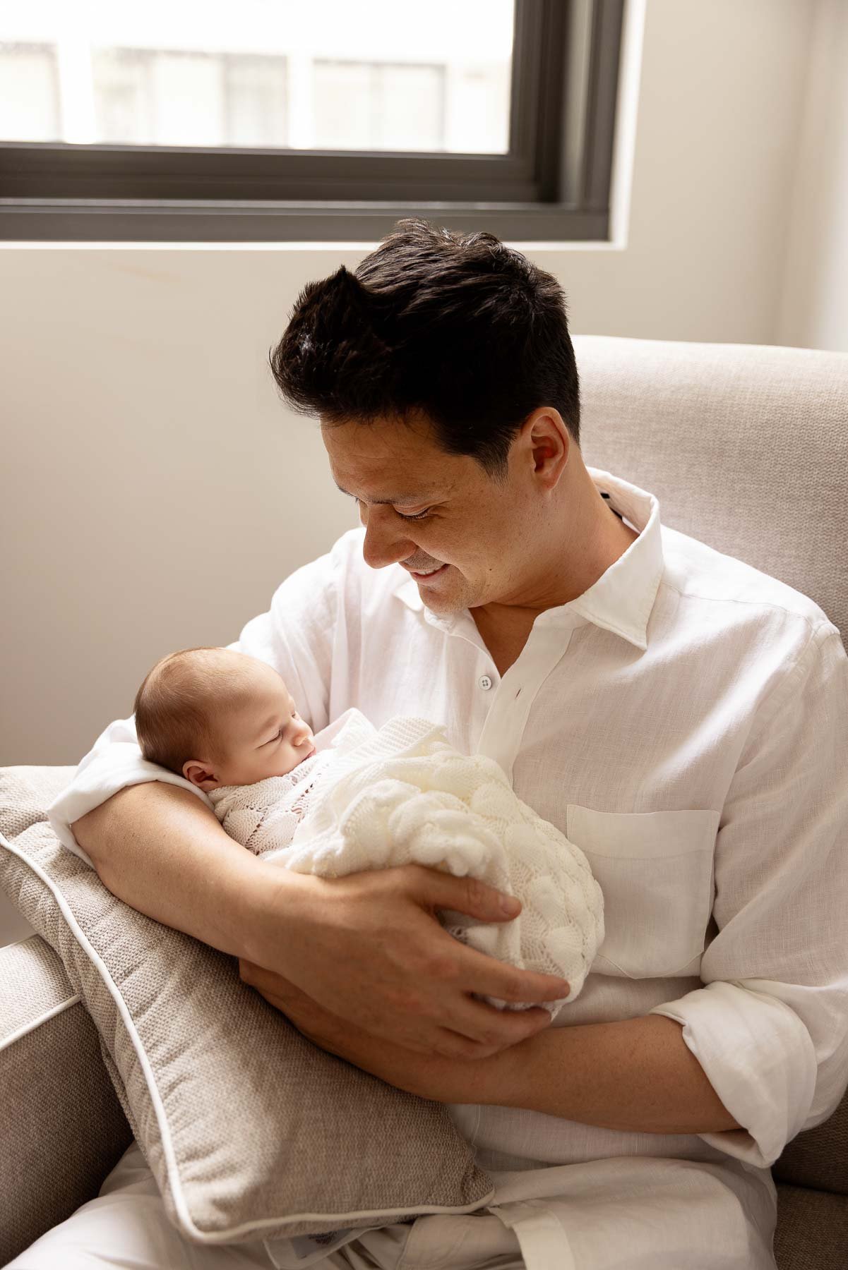 father holding his baby, wrapped in a white blanket, newborn photographer Sydney