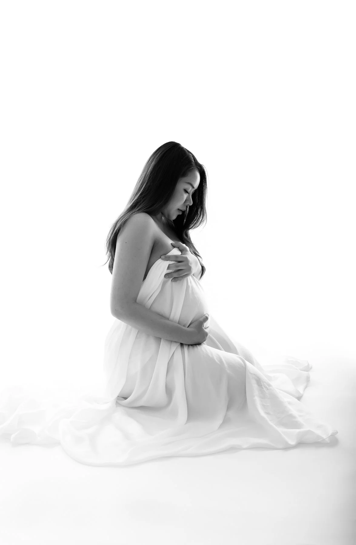 Black and white silhouette of a pregnant woman covered with sheer fabric, looking downwards.