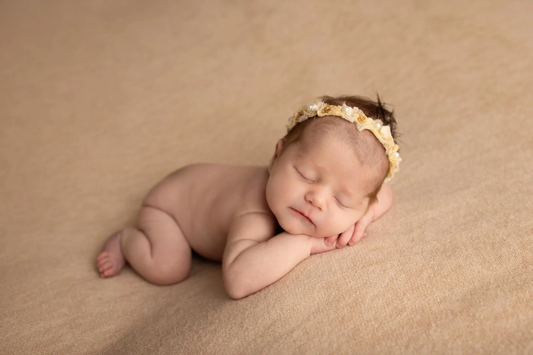 adorable nude newborn baby wearing a headband on a cream blanket
