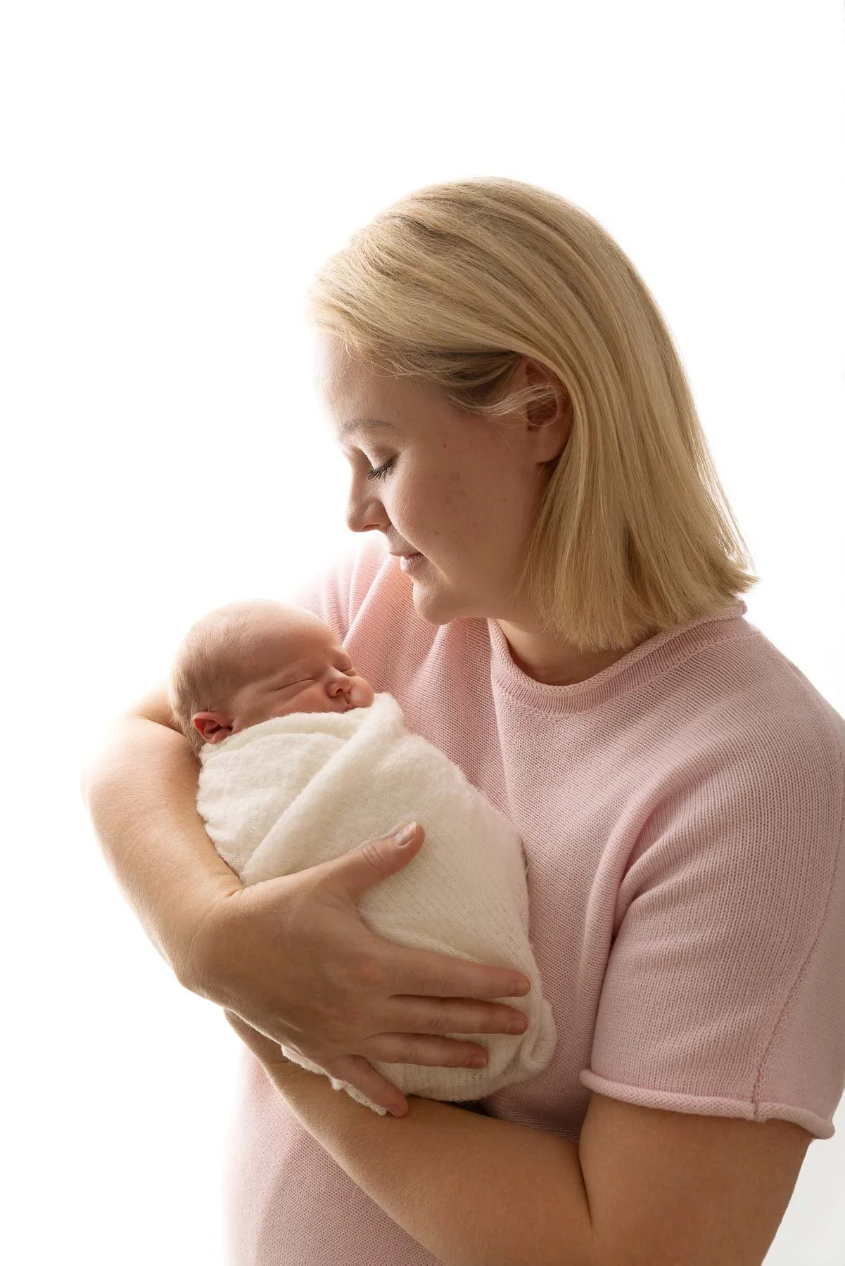 Mother holding a sleeping baby wrapped in a white blanket.